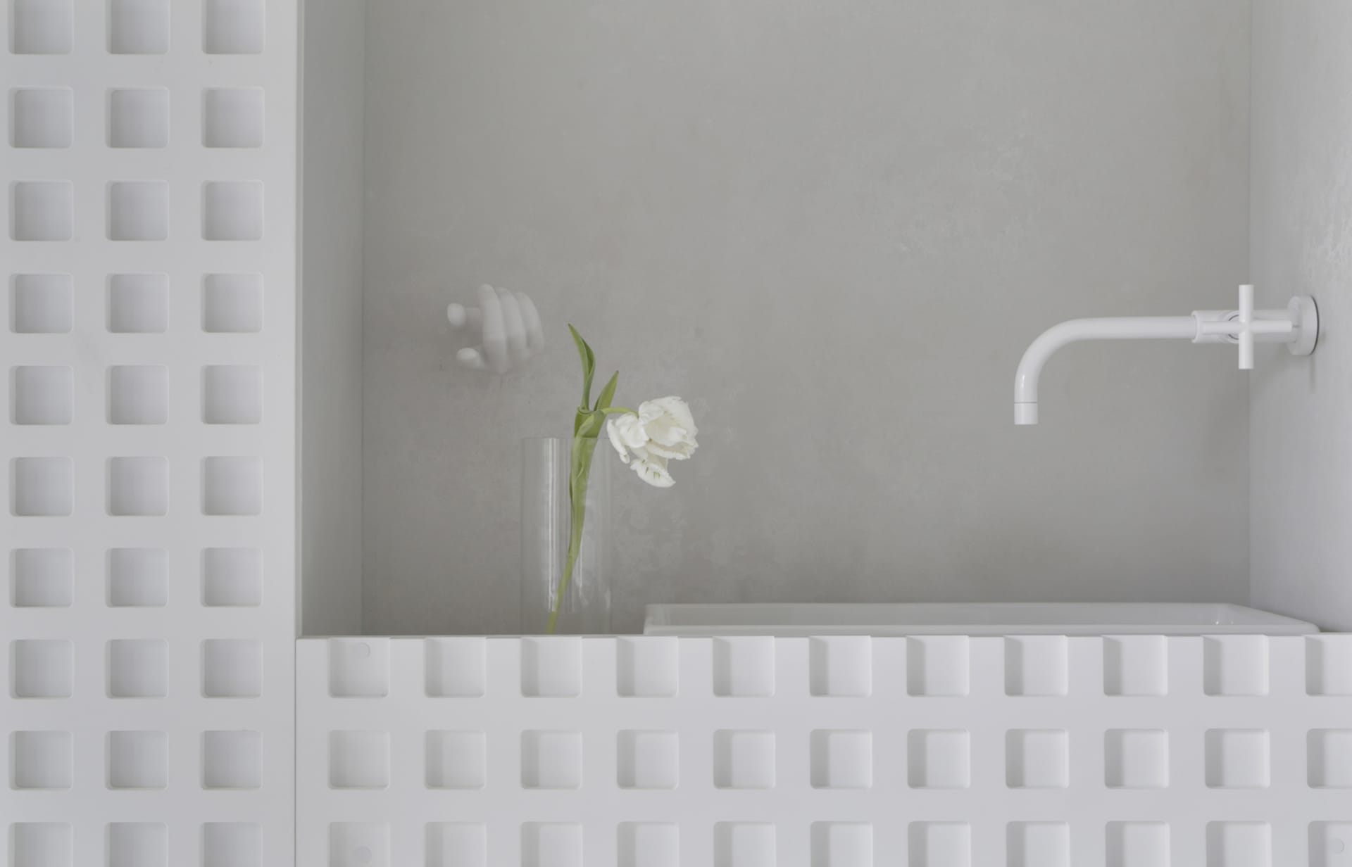 A minimalist modern bathroom with concrete walls, a white bathtub, and a white vase with a white flower on the edge of the tu