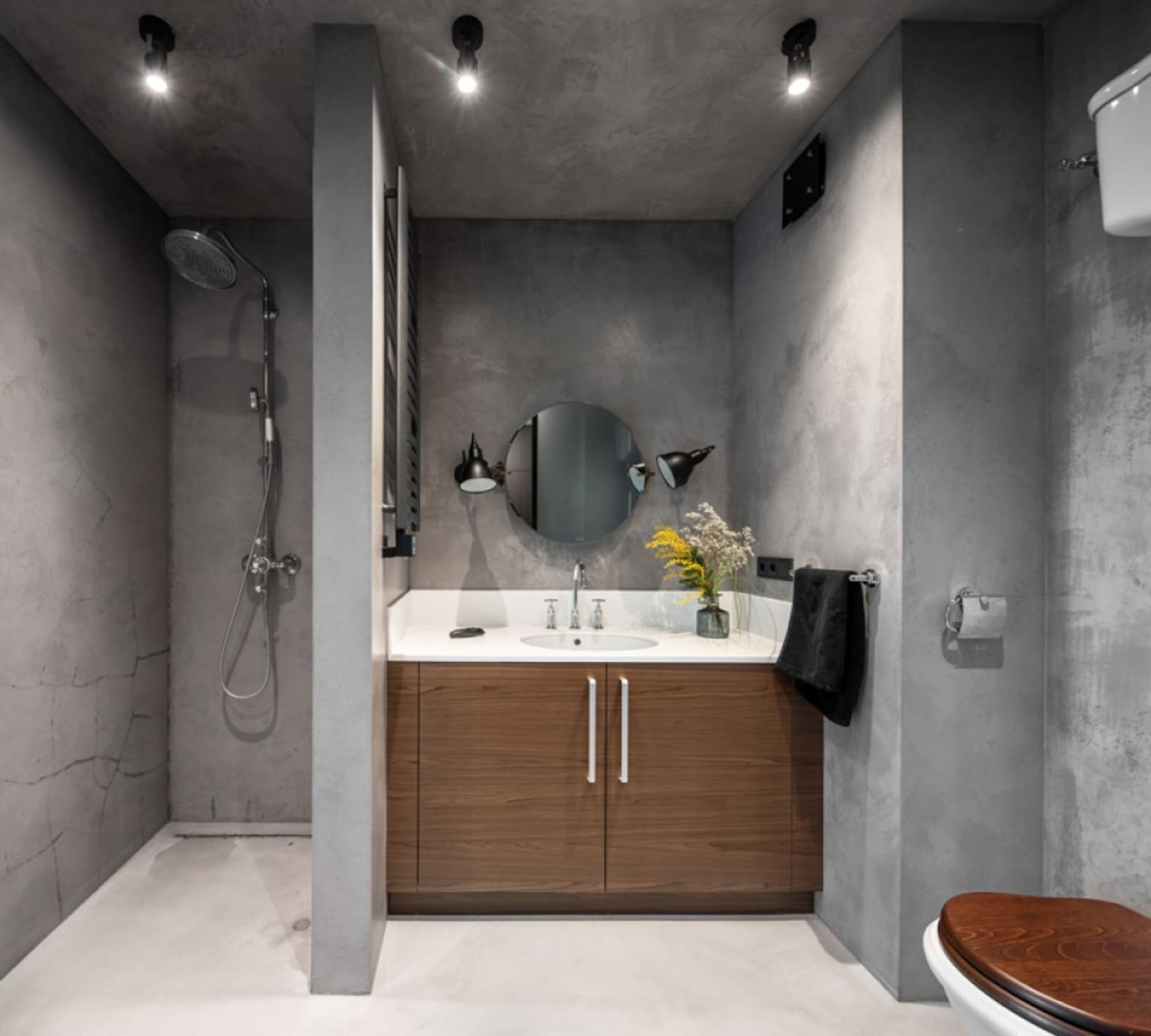 A modern bathroom with concrete walls, a wooden vanity, and industrial-style lighting.