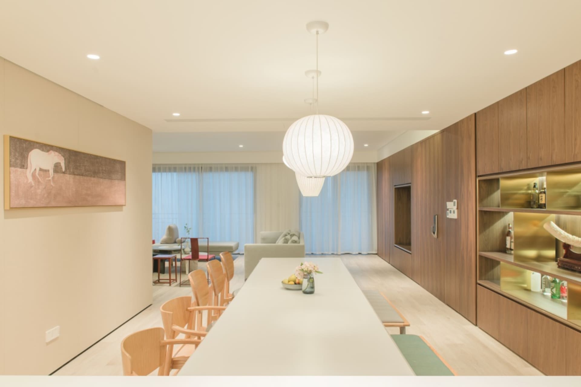 現代客廳兼餐廳,搭配木製餐椅、玻璃窗,以及懸掛在長餐桌上方的一盞白色吊燈。