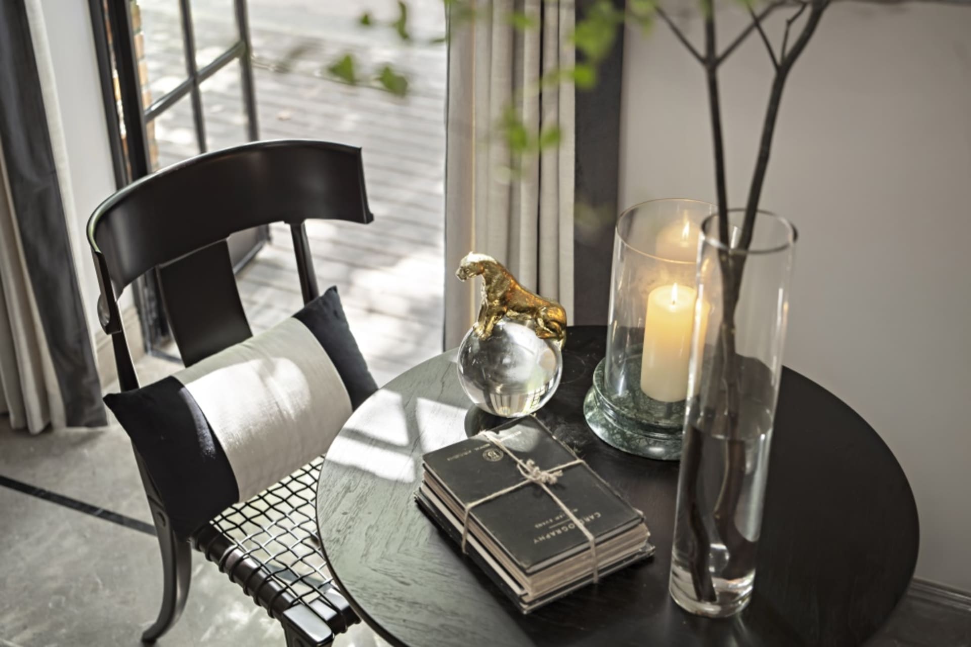 A glass side table with decorative items including a gold sculpture of a panther on a crystal ball, a candle in a glass holde