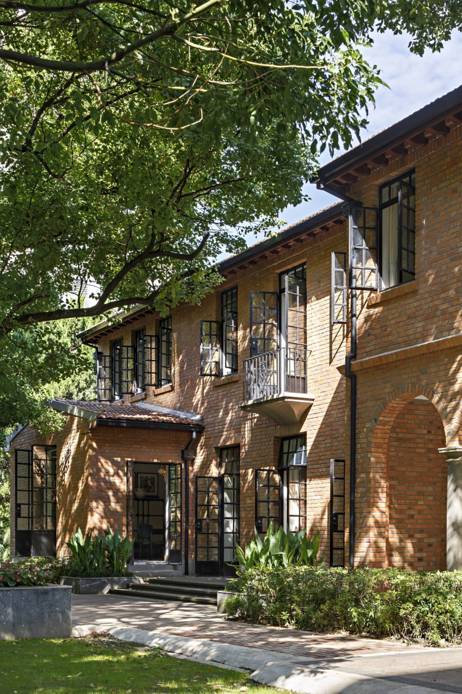 Modern residential house with brick and concrete exterior, featuring a garden with greenery and trees.