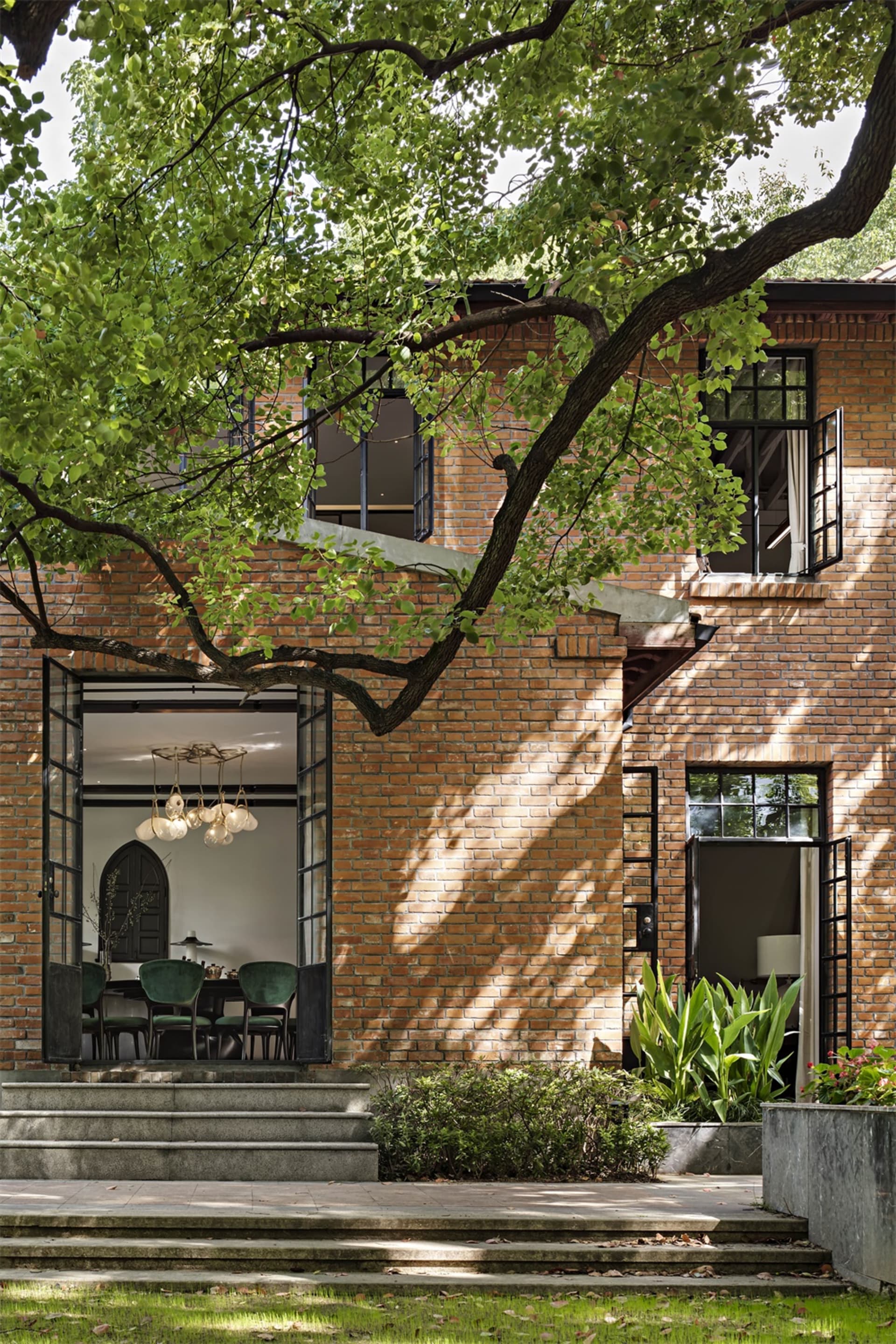 Modern house exterior made of brick with visible interior space through an open door, surrounded by greenery.