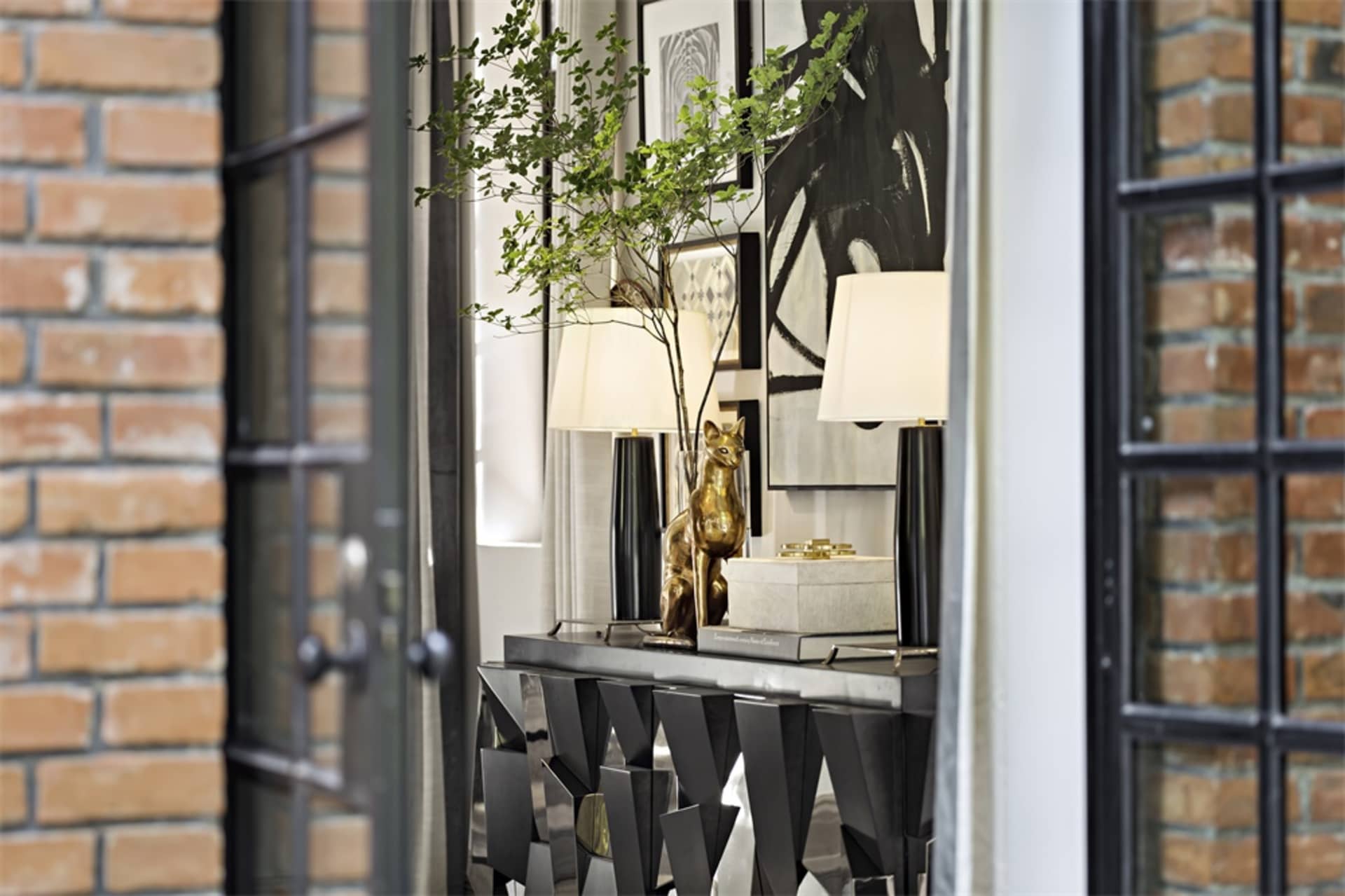 A modern interior console table with a metal base, a small potted green plant, and decorative items on top.