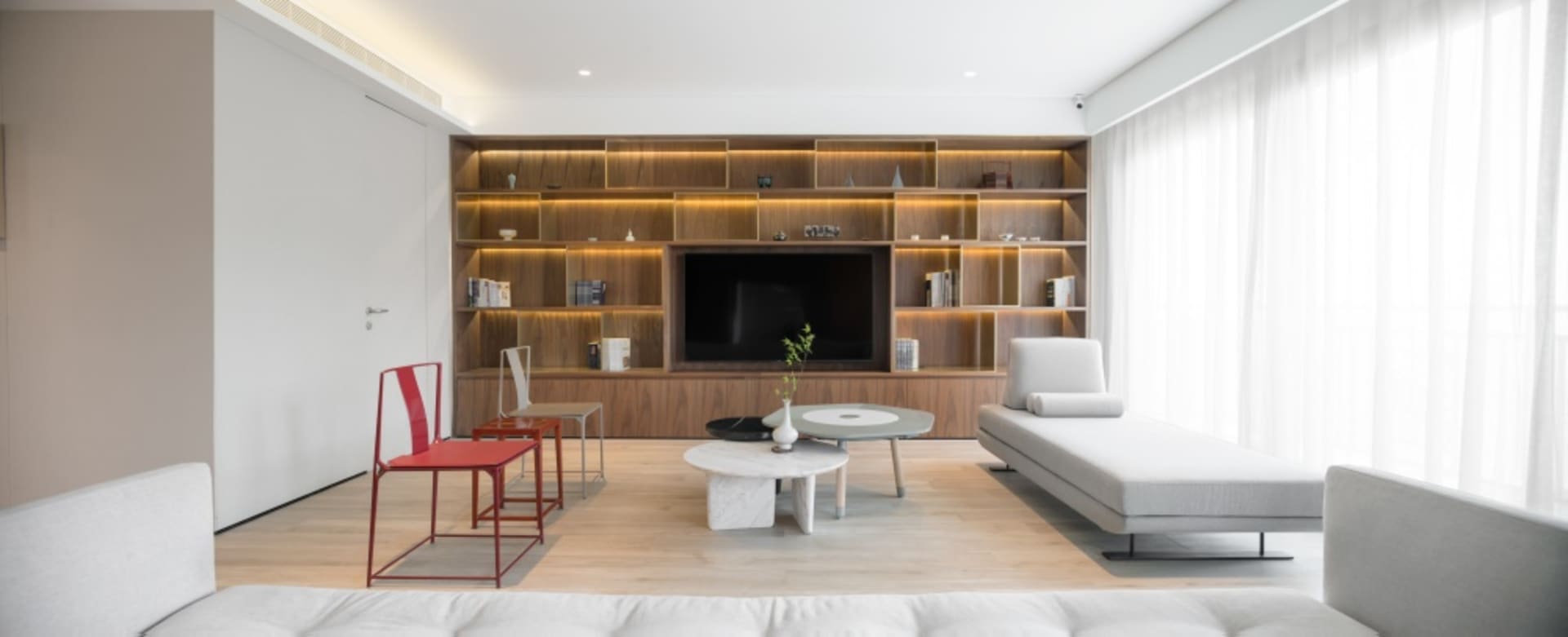 A modern minimalist living room featuring wooden shelves and fabric seating.