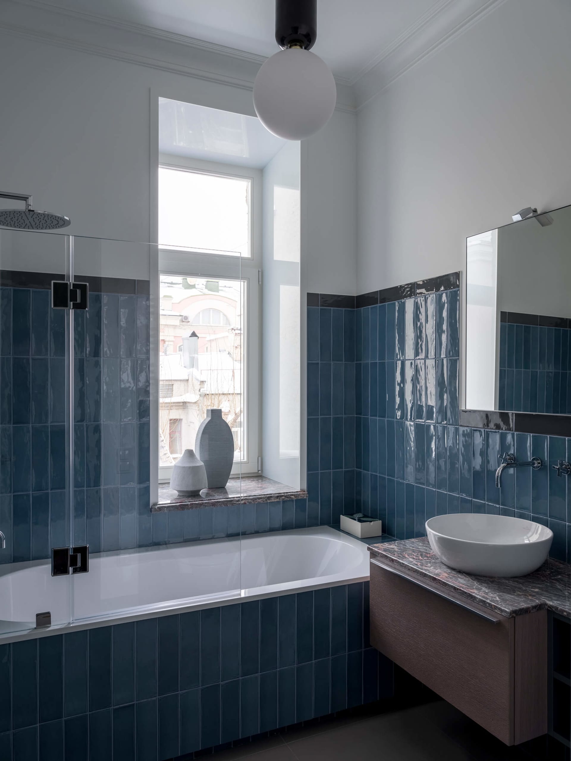 Modern bathroom with blue tiles, bathtub, sink, and window with natural light.