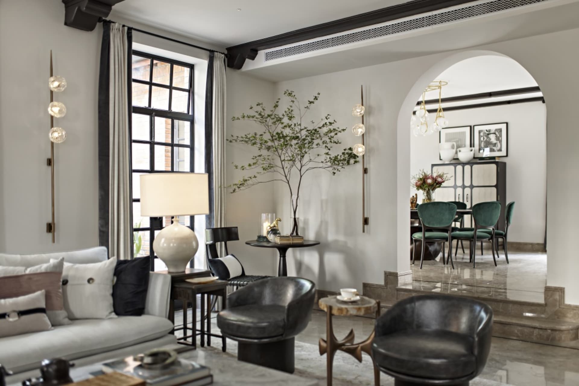 Modern living room with marble and glass decor, featuring a grey sofa, black chairs, and a glass table.