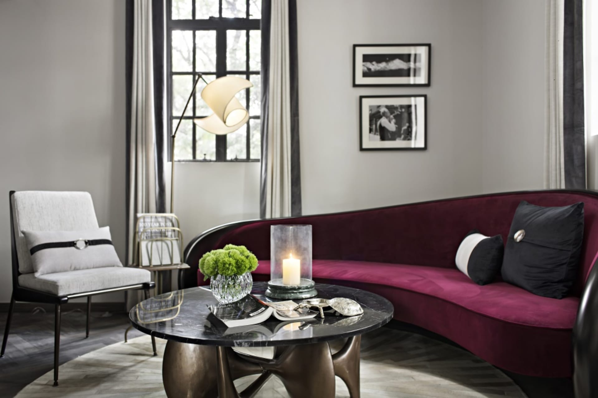 A modern living room featuring a dark, curved velvet sofa with marble accents, a marble coffee table, and a white armchair un