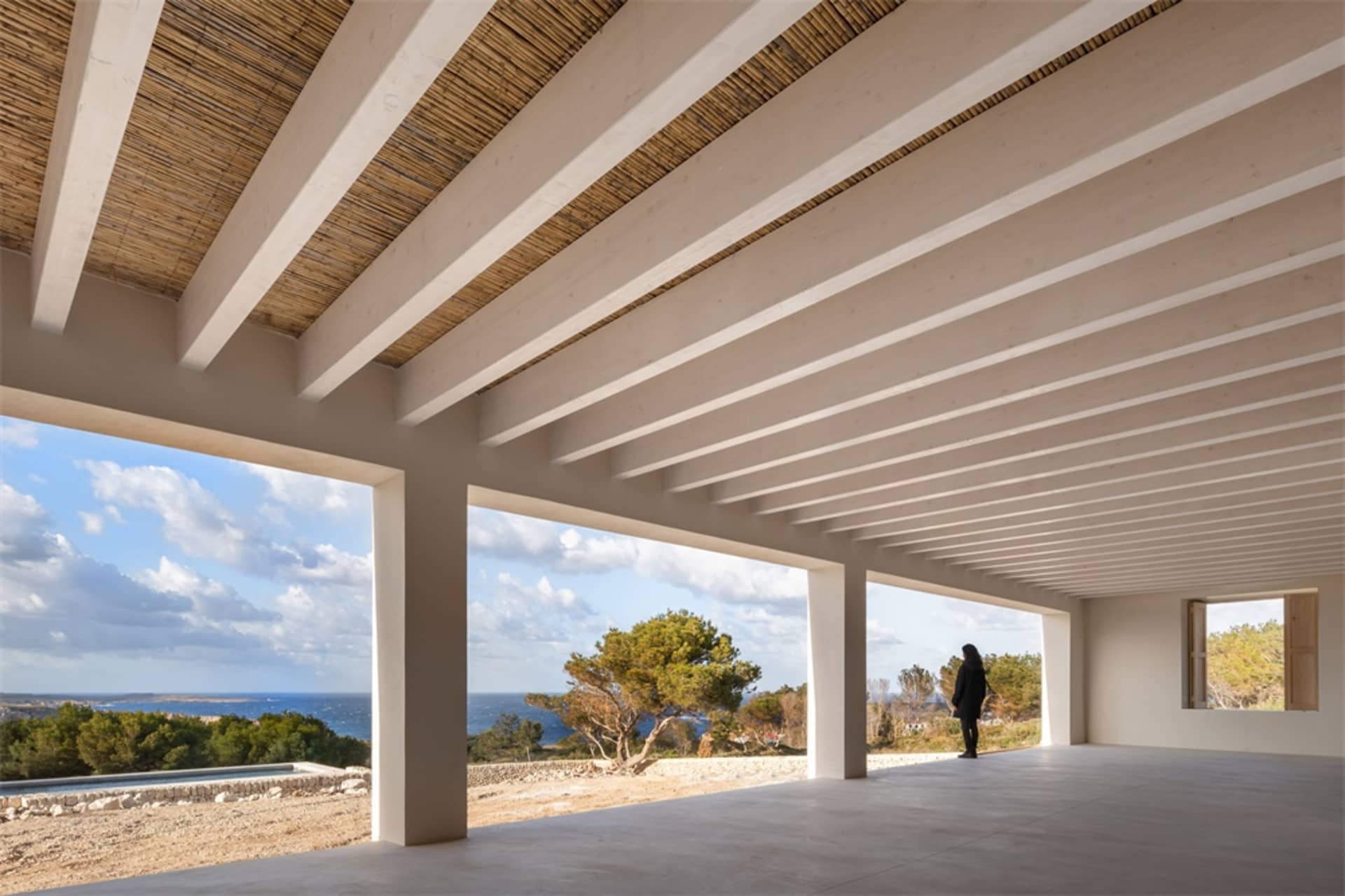 Modern residential interior featuring a spacious patio overlooking the ocean with wooden ceiling beams and concrete flooring.