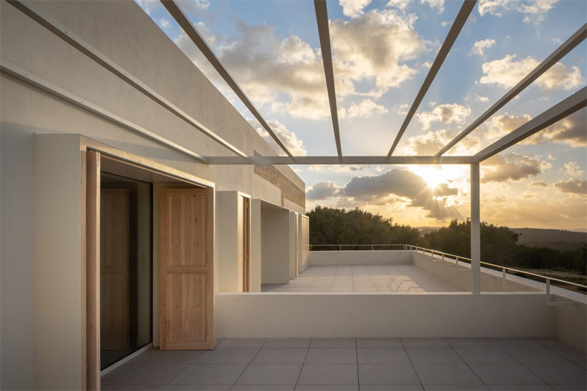 A modern terrace featuring concrete floors and walls with a view of lush greenery at sunset.