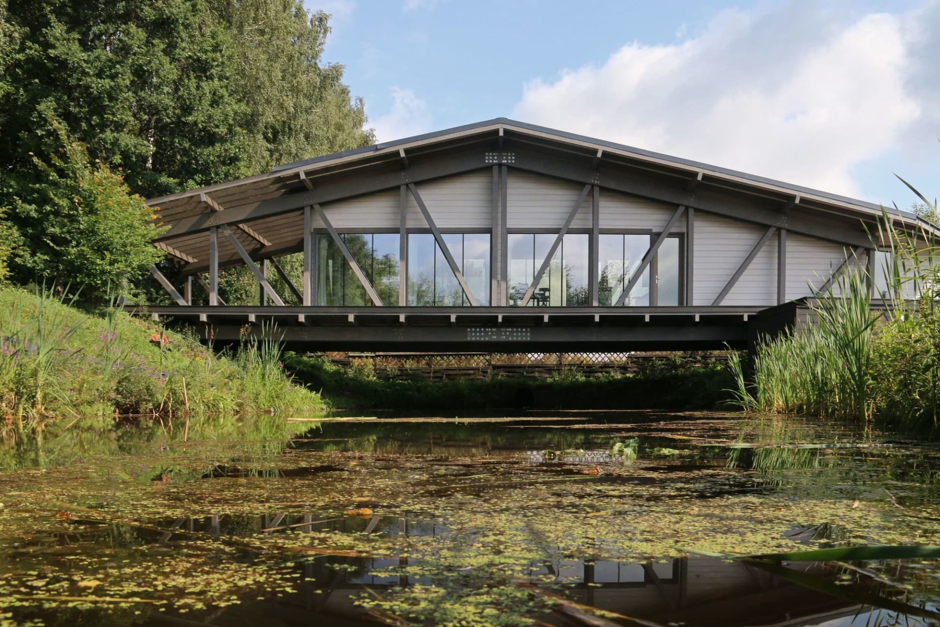 Modern residential architecture featuring a steel and glass bridge crossing a river.
