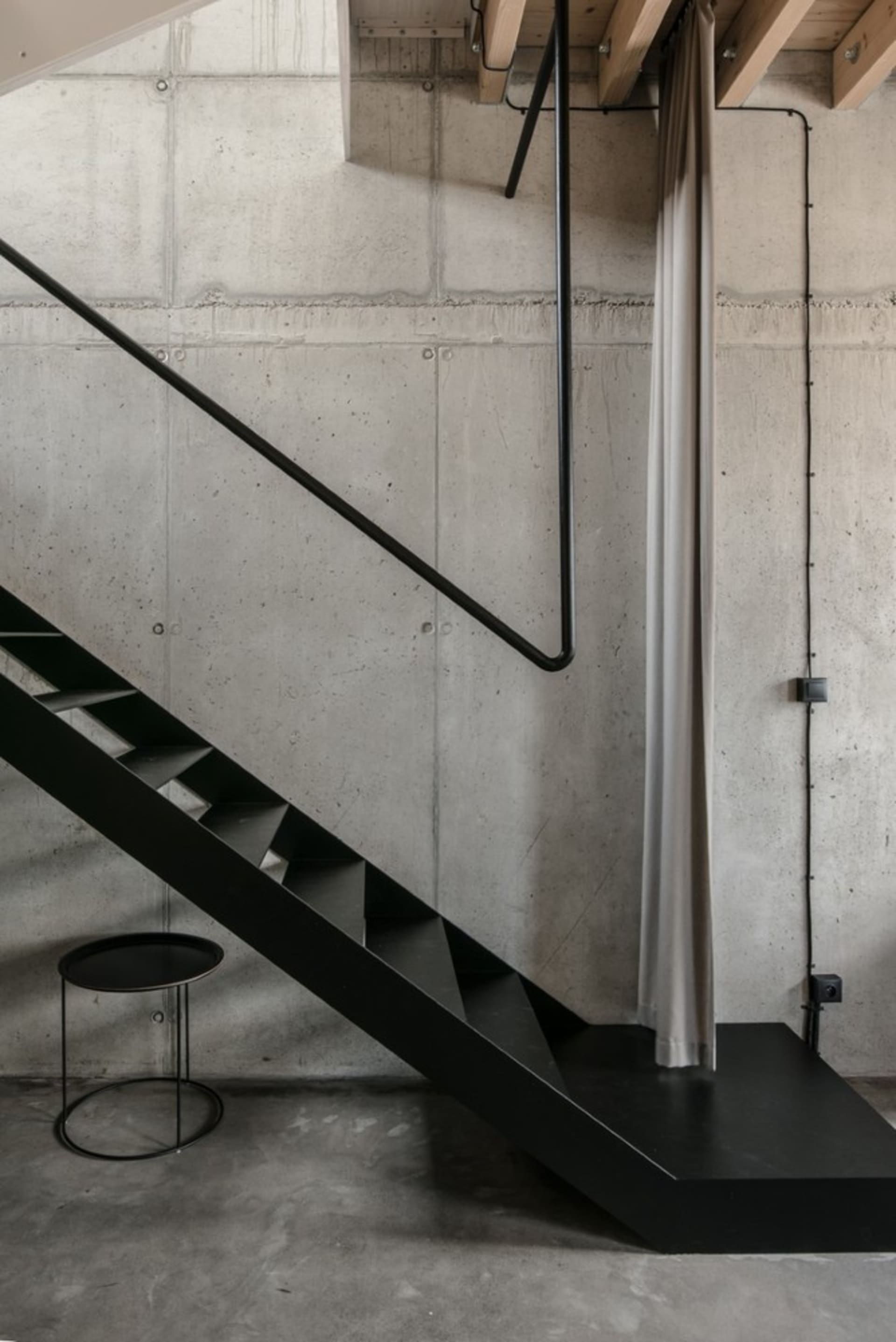 Modern industrial staircase with black metal railing and concrete steps against a raw concrete wall.