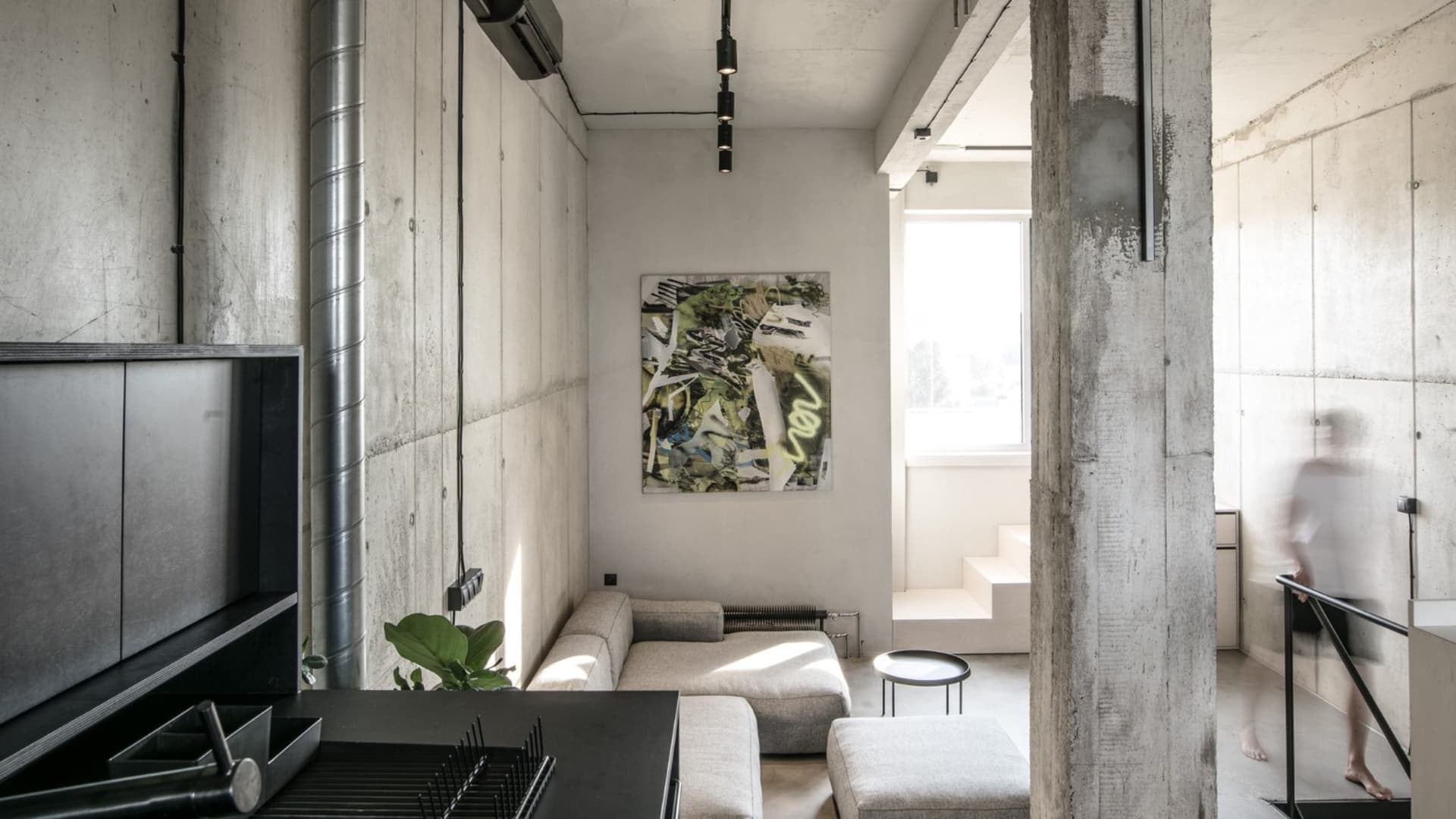 Modern minimalist living room with concrete walls and a grey sectional sofa.