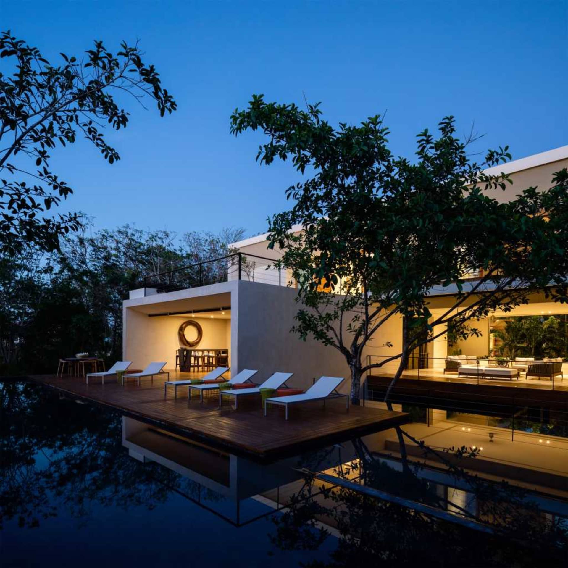 Modern house with glass walls and wooden deck overlooking pool at night.