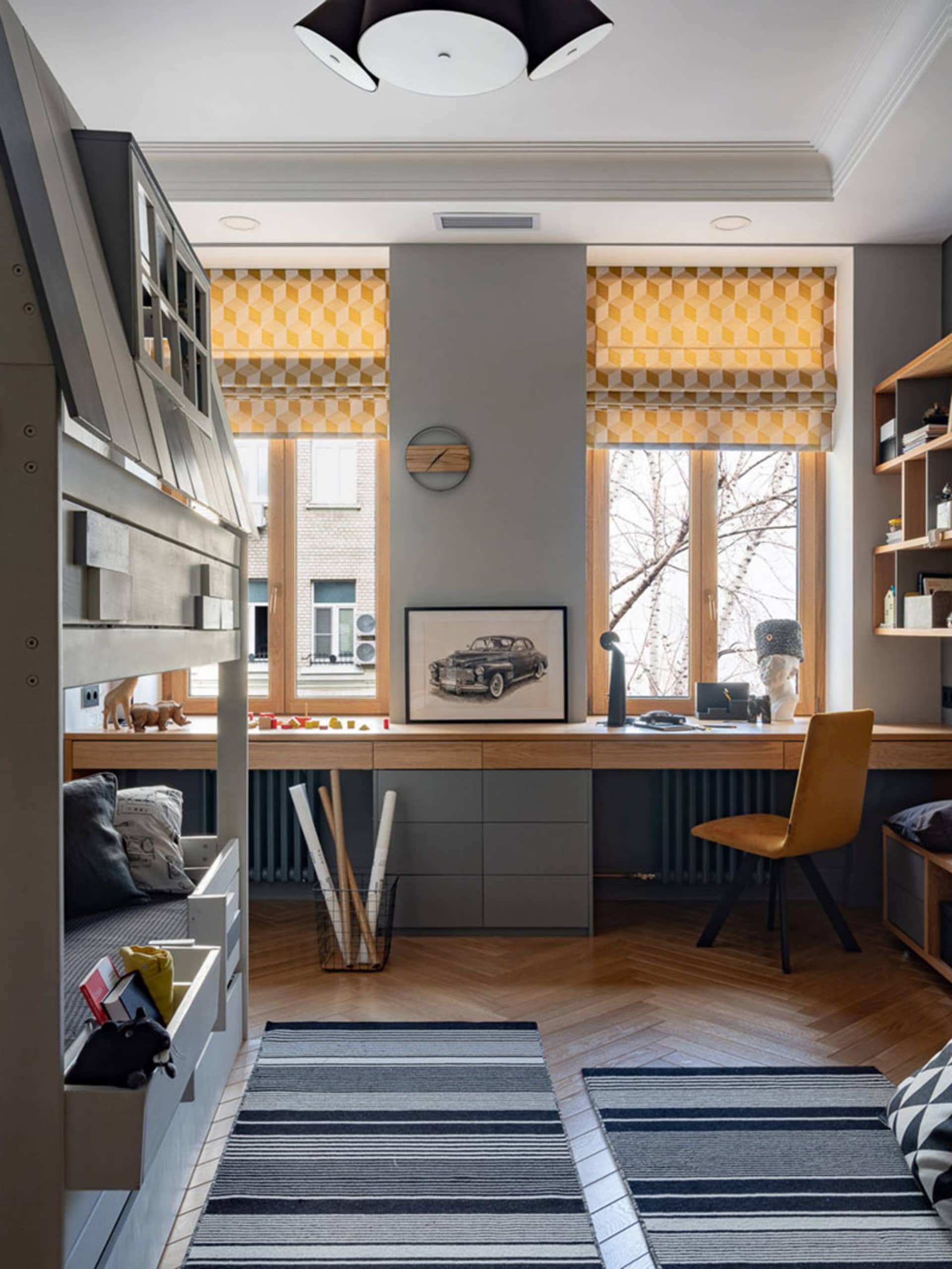 Minimalist home office with a wooden desk, yellow geometric window shades, and a grey and white striped rug.