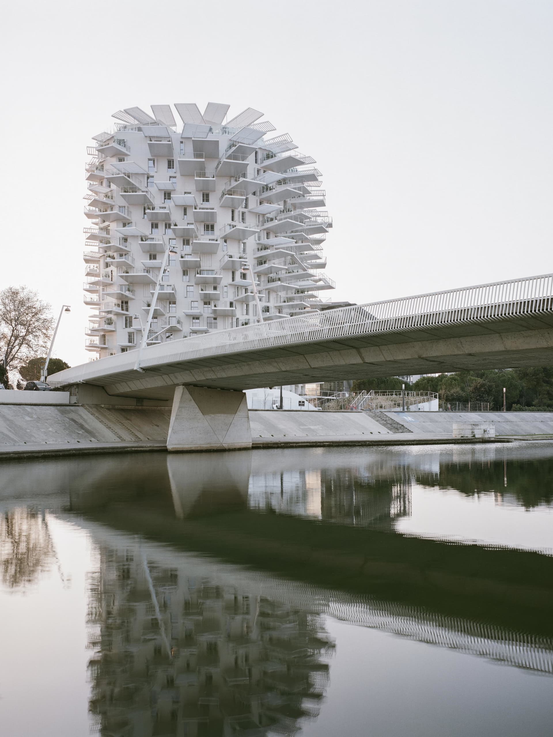 Concrete building with geometric balconies reflected in calm river waters, modern architectural style.