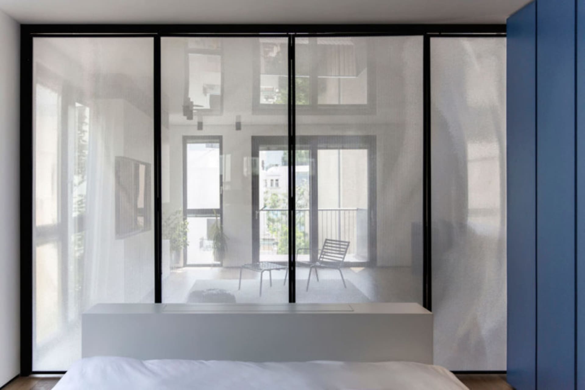 A modern bedroom featuring a large glass wall that provides a view of the outside and allows natural light to flood the space