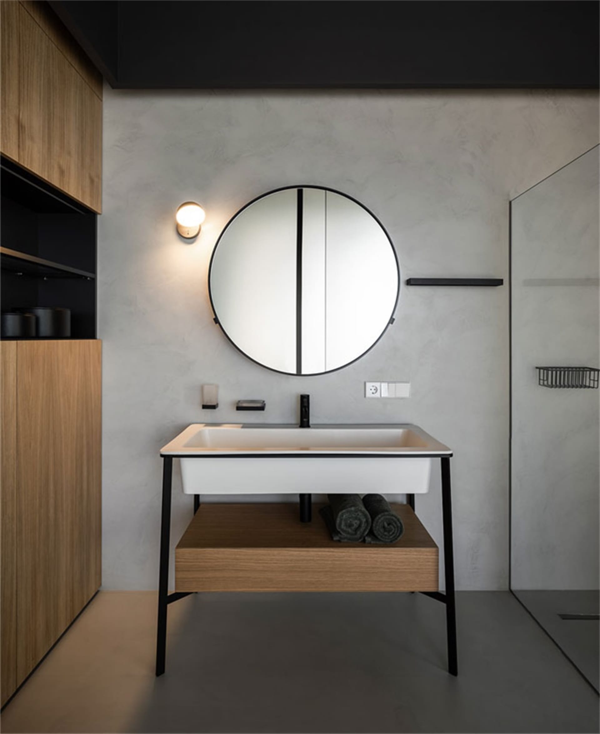Modern minimalist bathroom featuring a white sink with a black faucet, wooden shelves, and a round mirror.