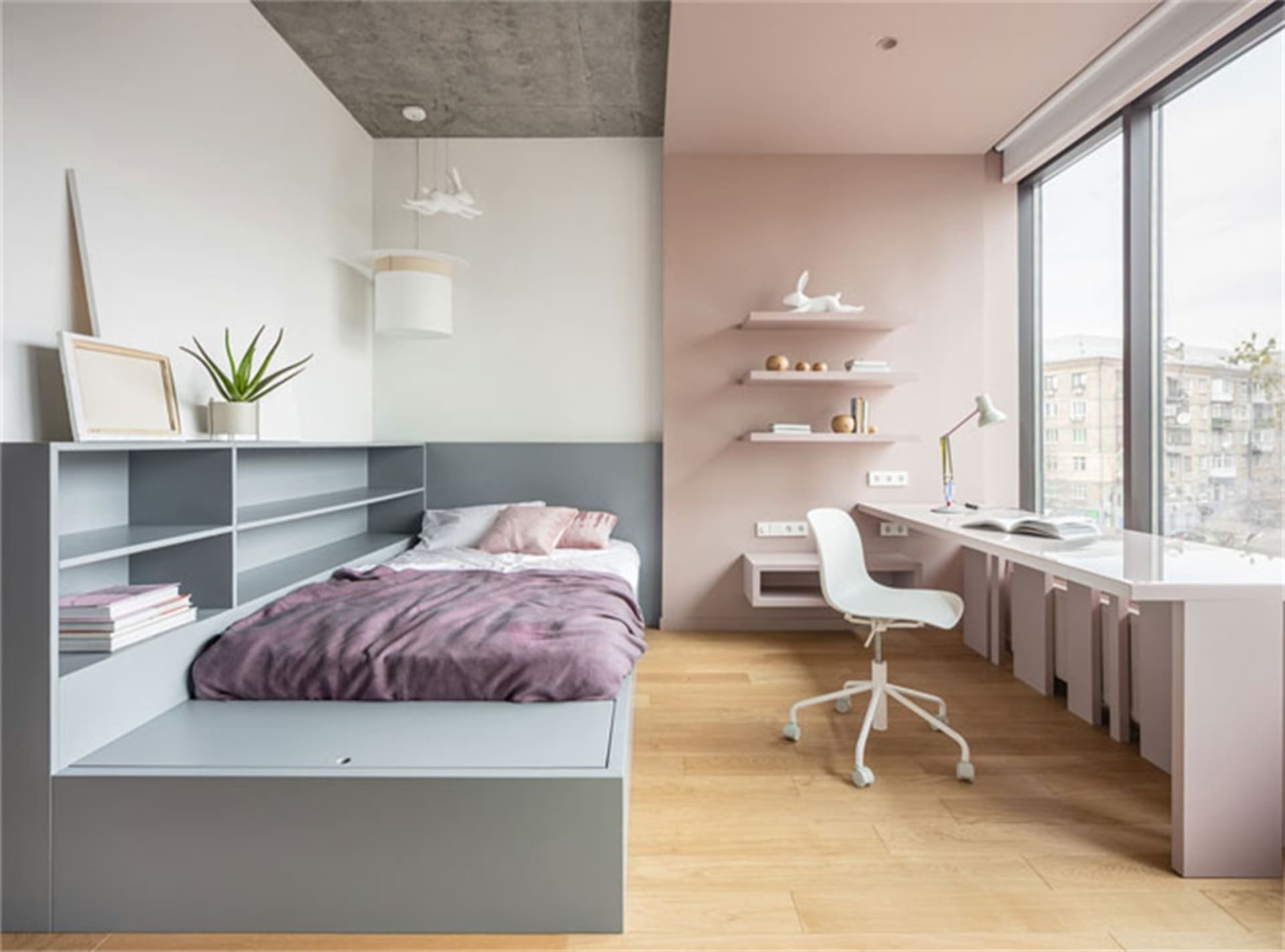 A modern minimalist bedroom with a concrete ceiling, a grey bed platform with built-in storage, a pink and grey bedding set,