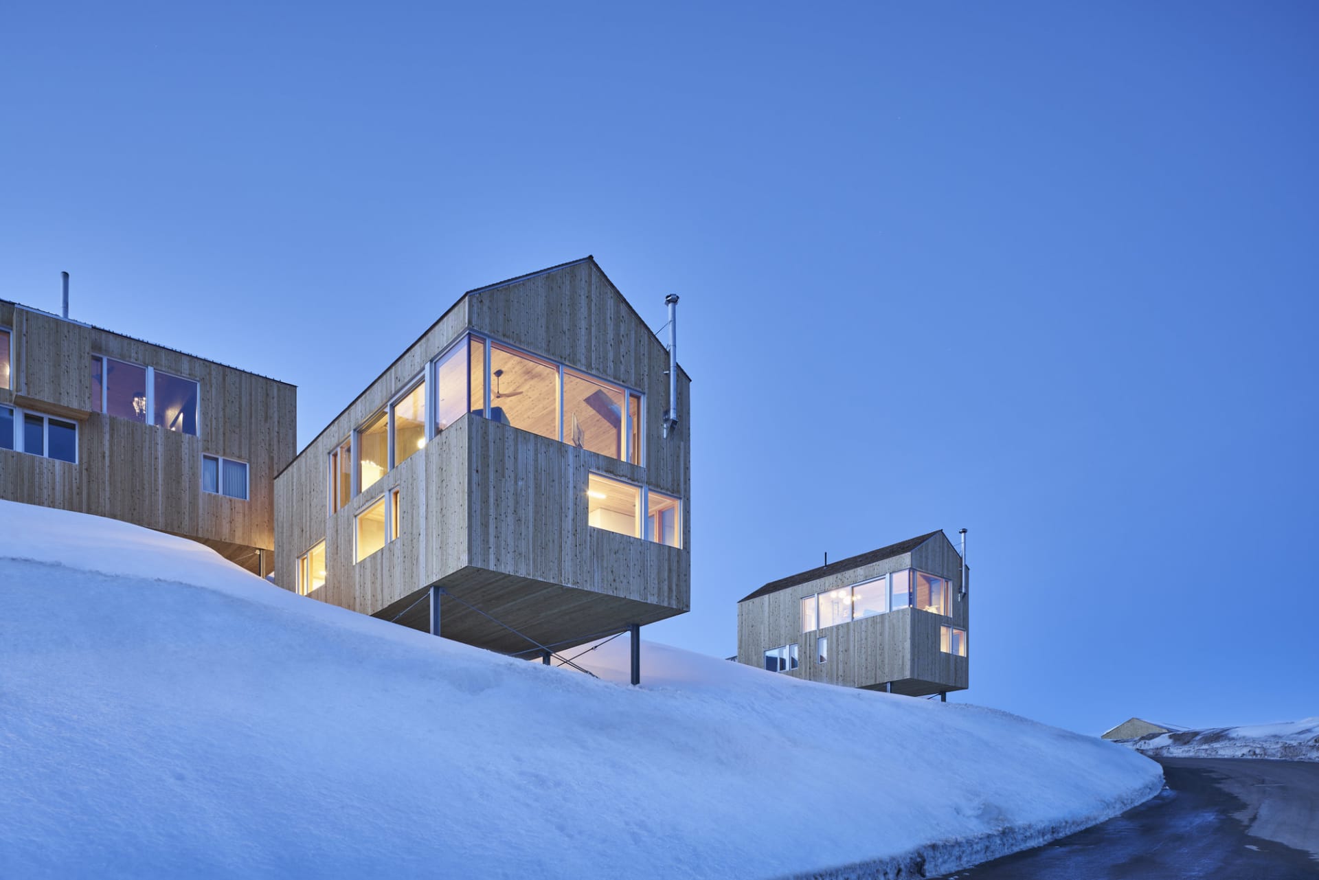Modern residential buildings with wooden exterior and snow-covered ground at dusk