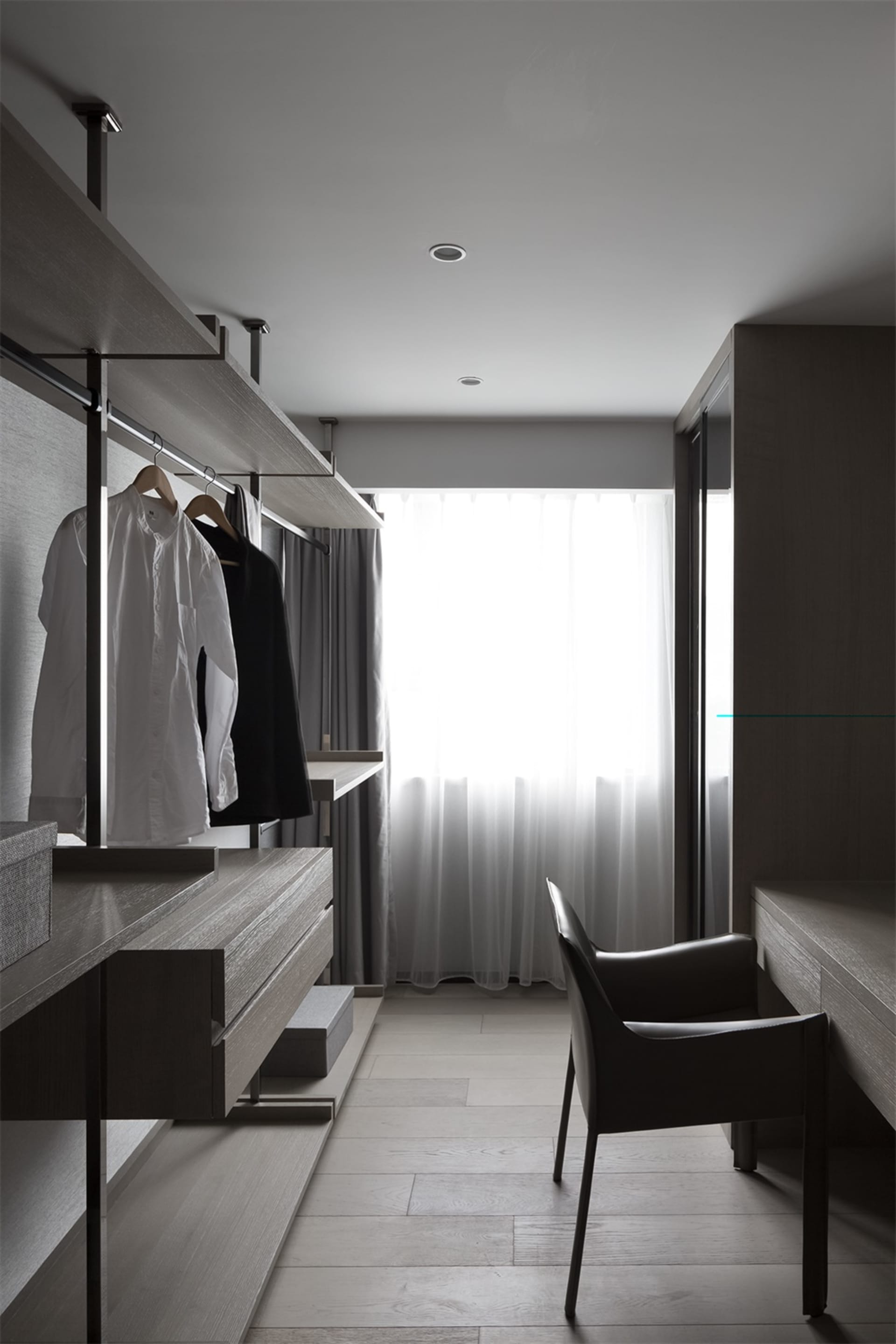 A minimalist closet with wooden shelves, white curtains, and a white chair by the window.