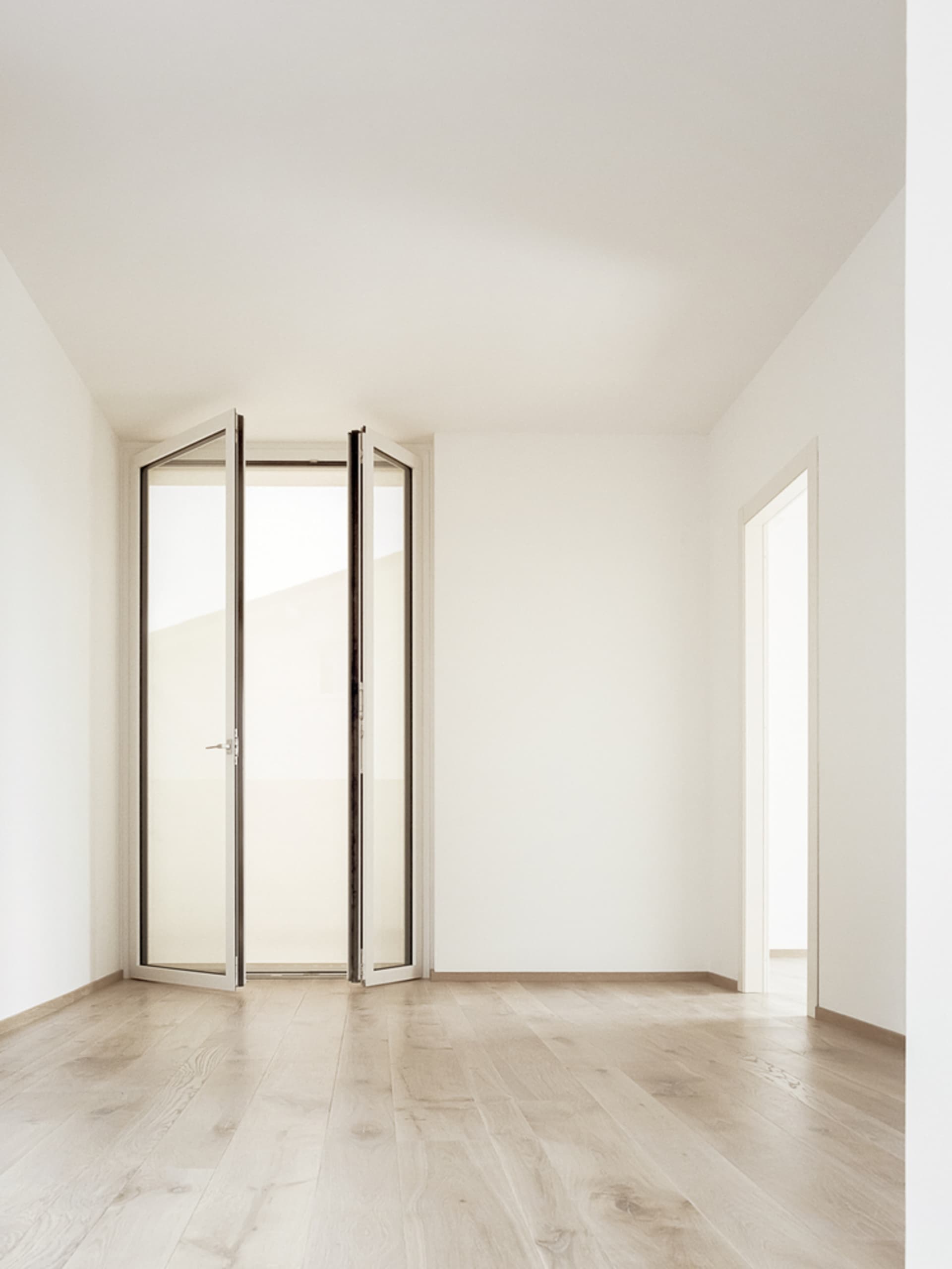 An empty room with minimalist design, featuring wood paneling and an open door leading to another room.