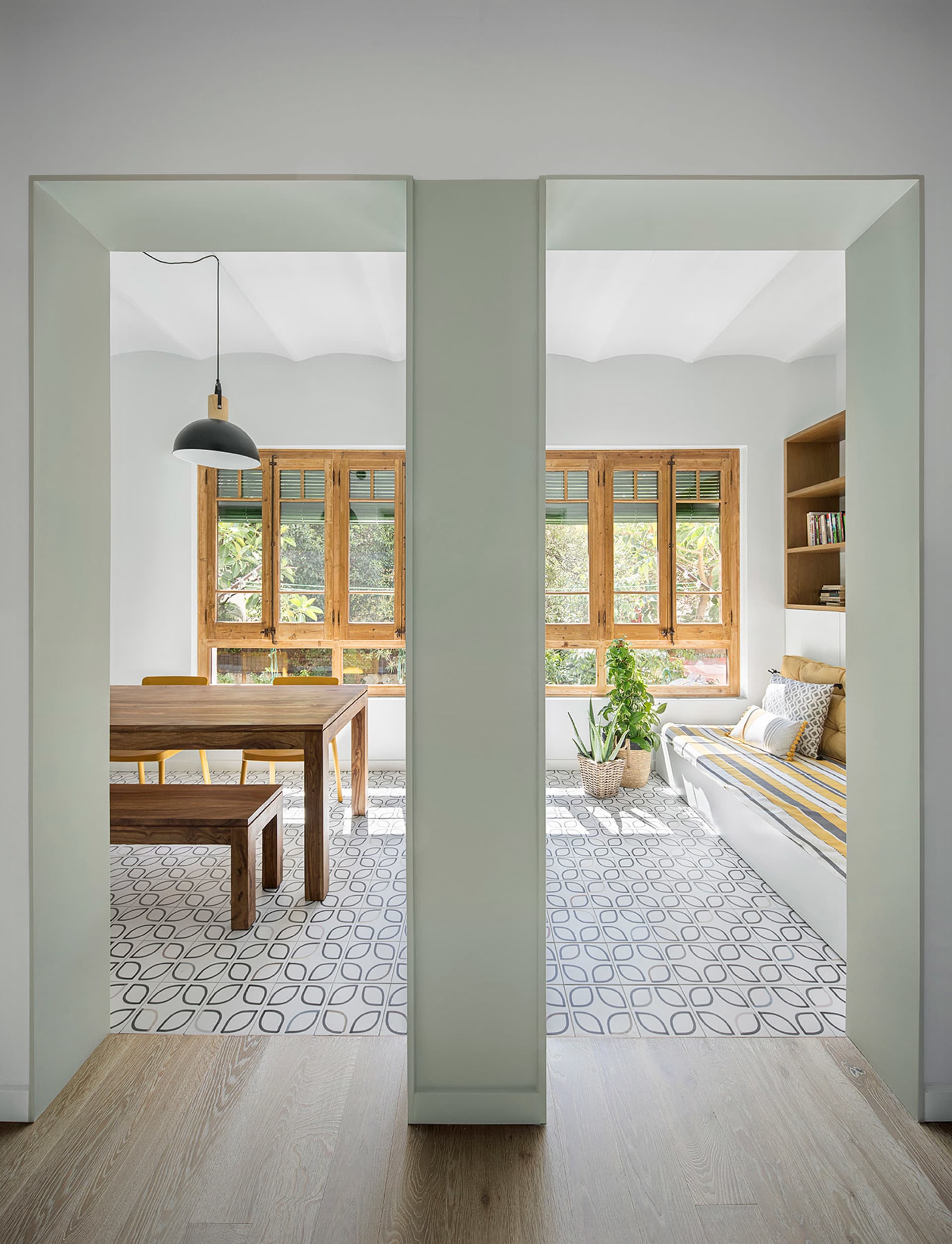 A minimalist residential living space featuring wood furniture, patterned tiles, and a cozy reading nook.