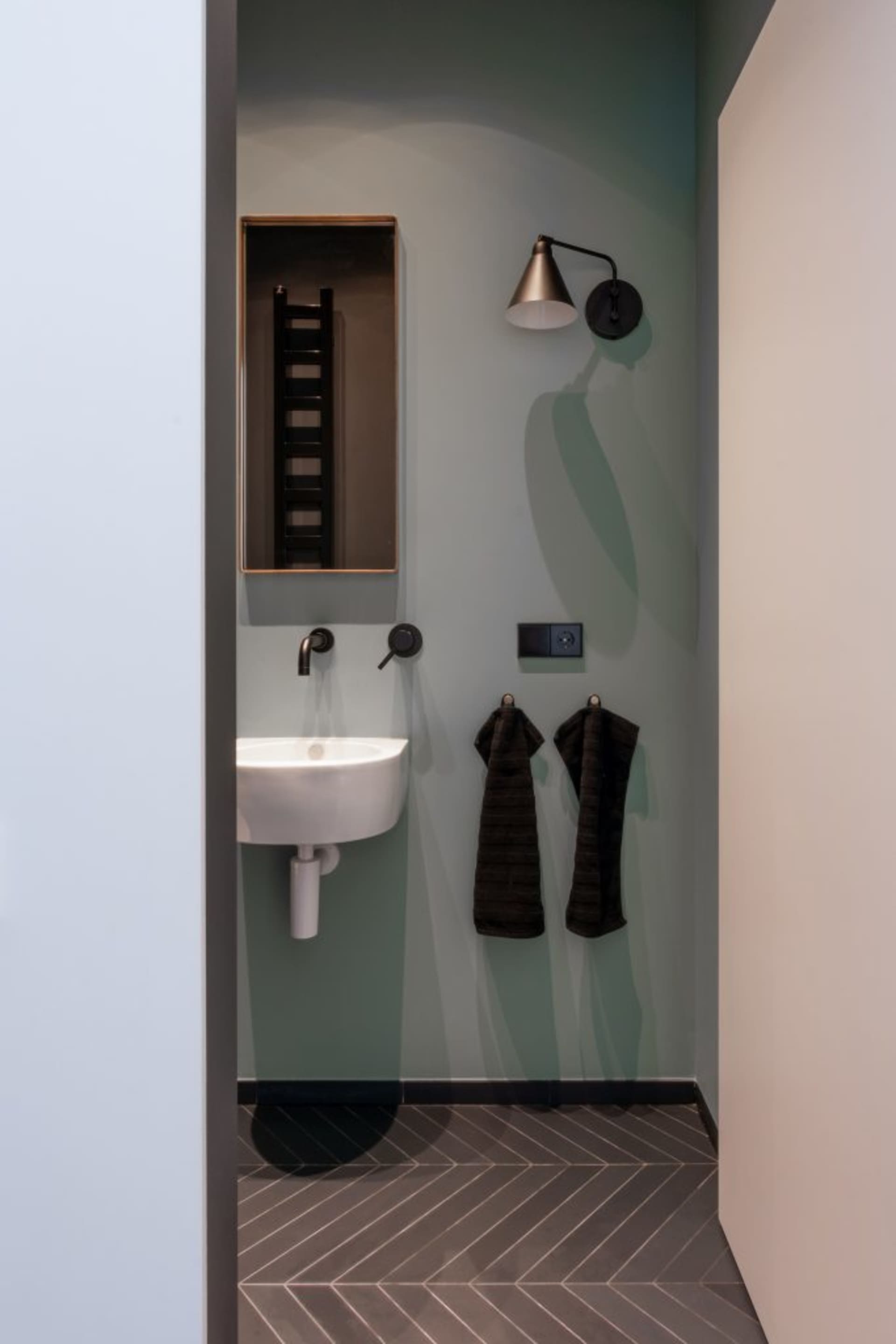 A modern concrete bathroom with a small sink, mirror, and towel hooks.