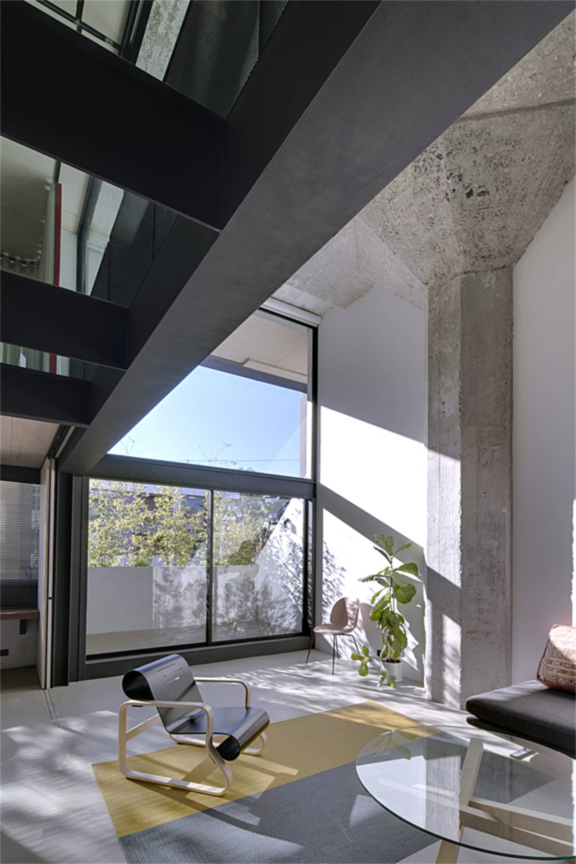 Modern industrial living room featuring concrete walls, glass windows, and minimalist furniture.