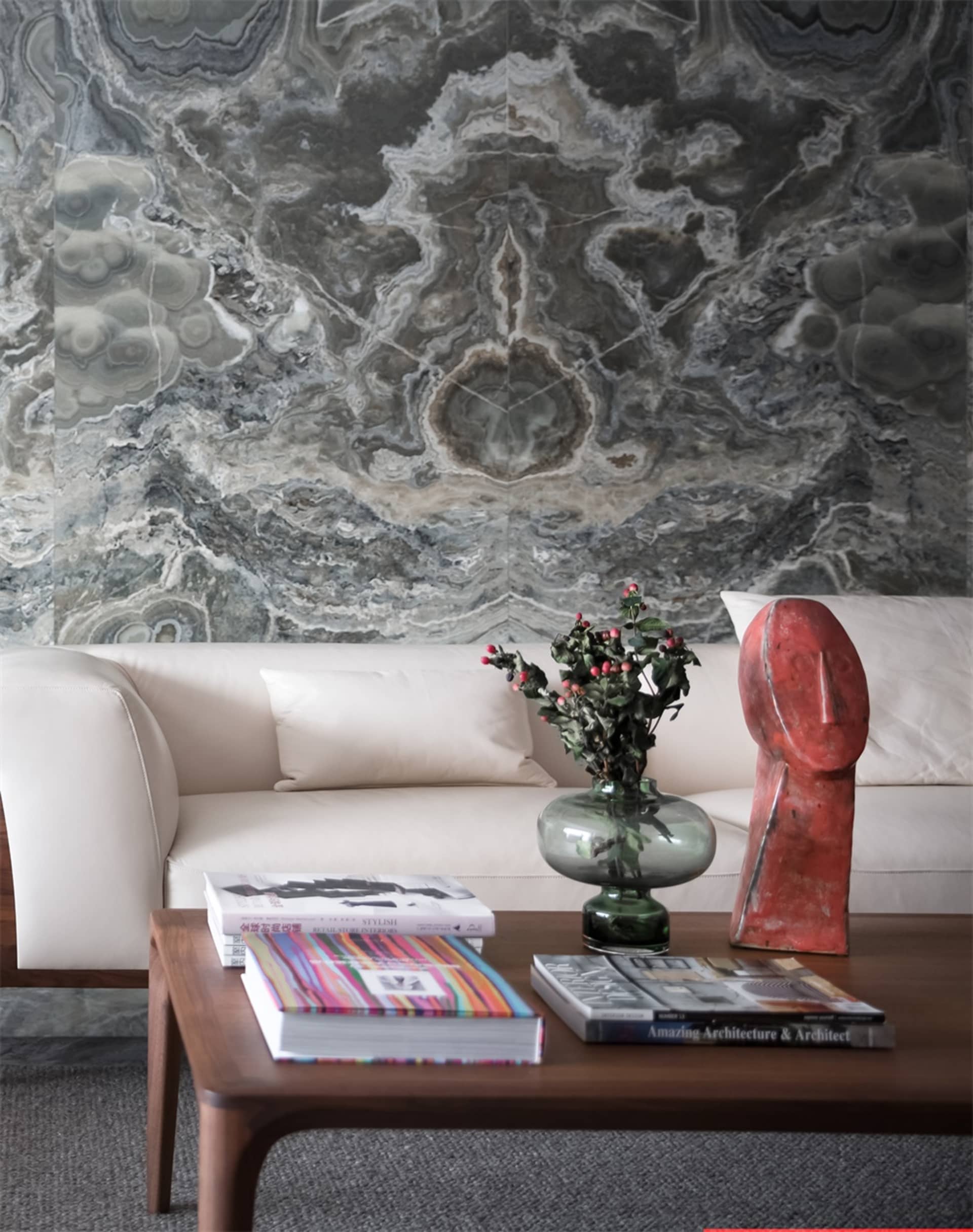 A modern living room featuring marble walls, a white leather sofa, and a wooden coffee table with books, a vase, and a sculpt