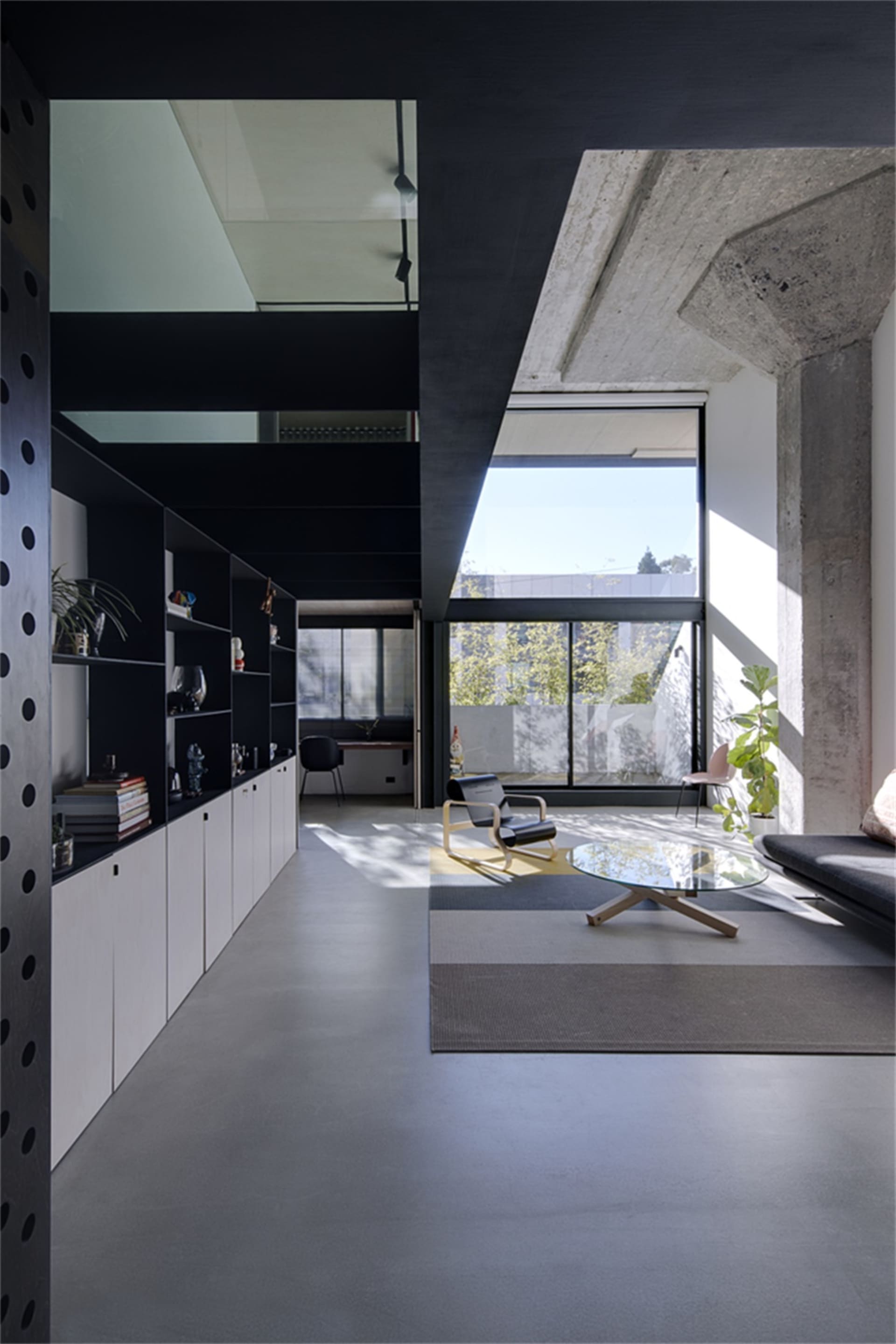 Modern living room with minimalist design featuring concrete flooring, glass coffee table, and industrial style furniture.