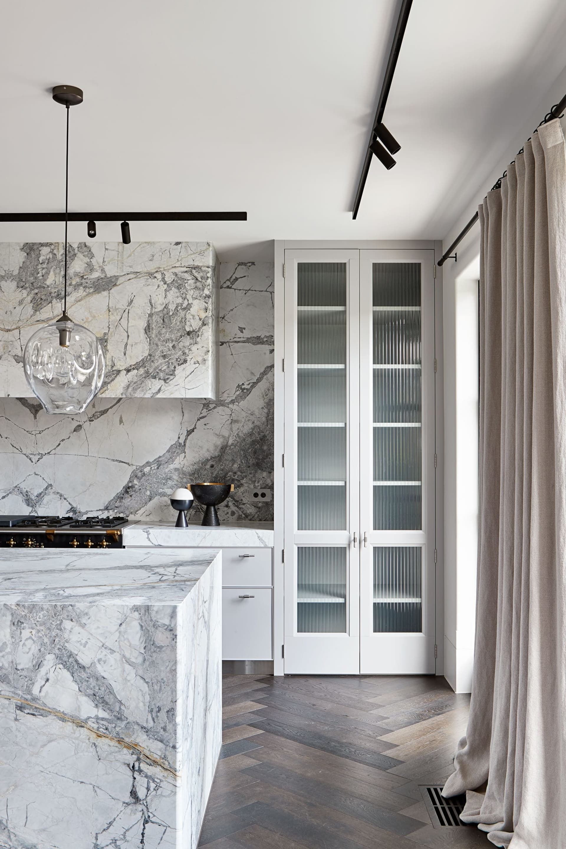 A modern kitchen with marble countertops and flooring, featuring white cabinetry and a minimalist design.