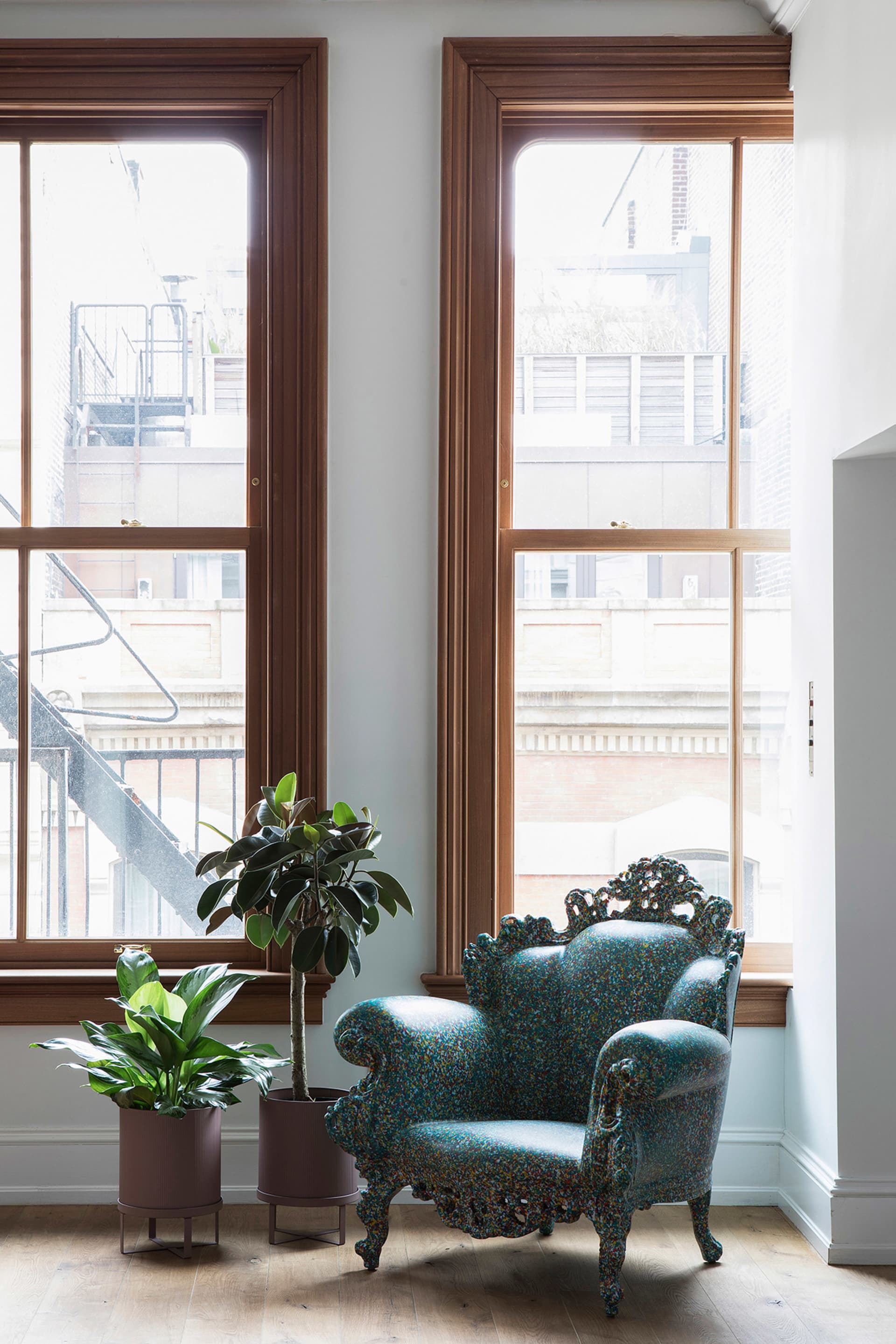 A modern, blue, scale-shaped armchair in a living space with a large window and plants.