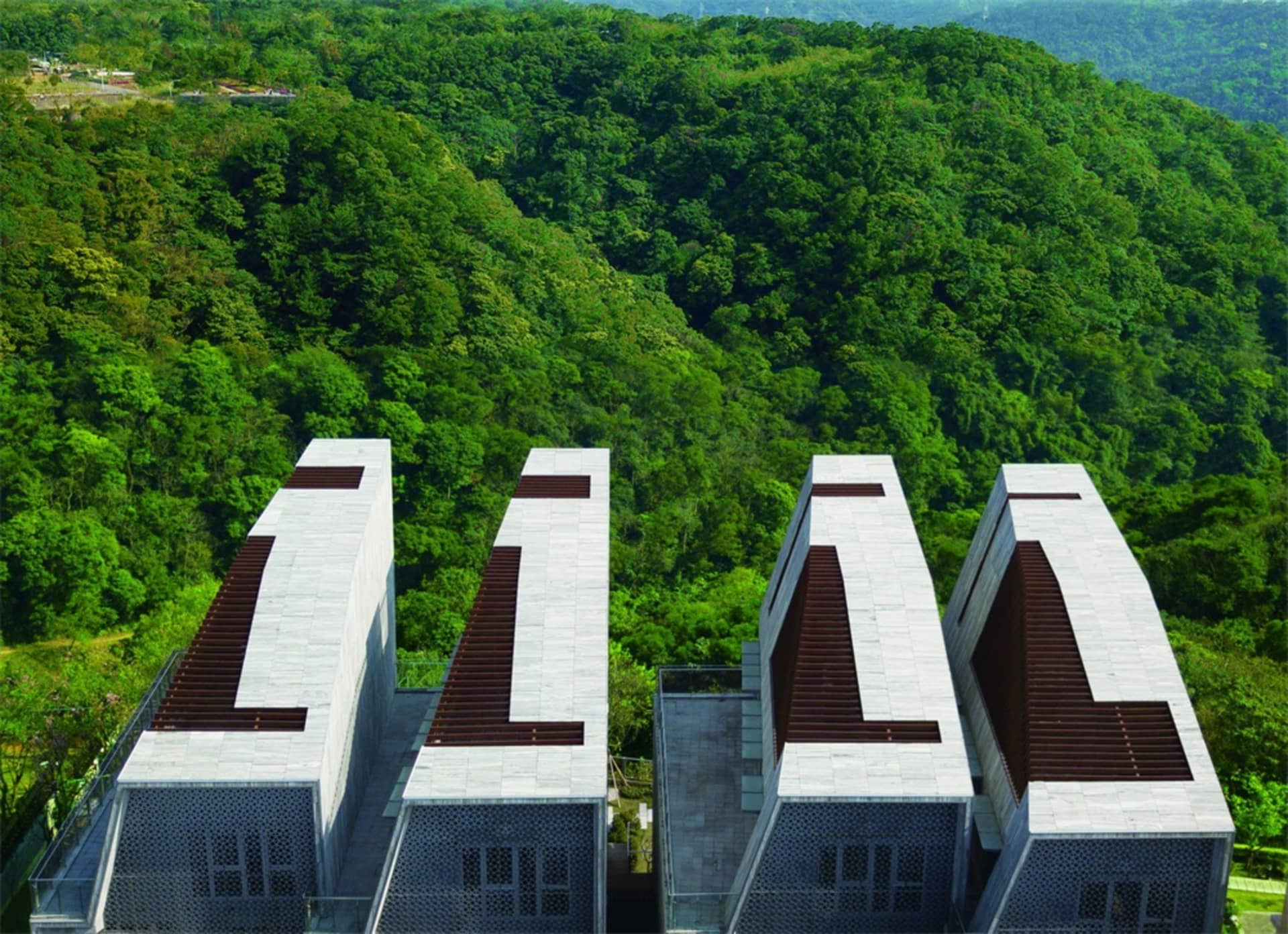 四棟現代水泥建築群坐落於山坡上,周圍環繞著茂密的綠意。