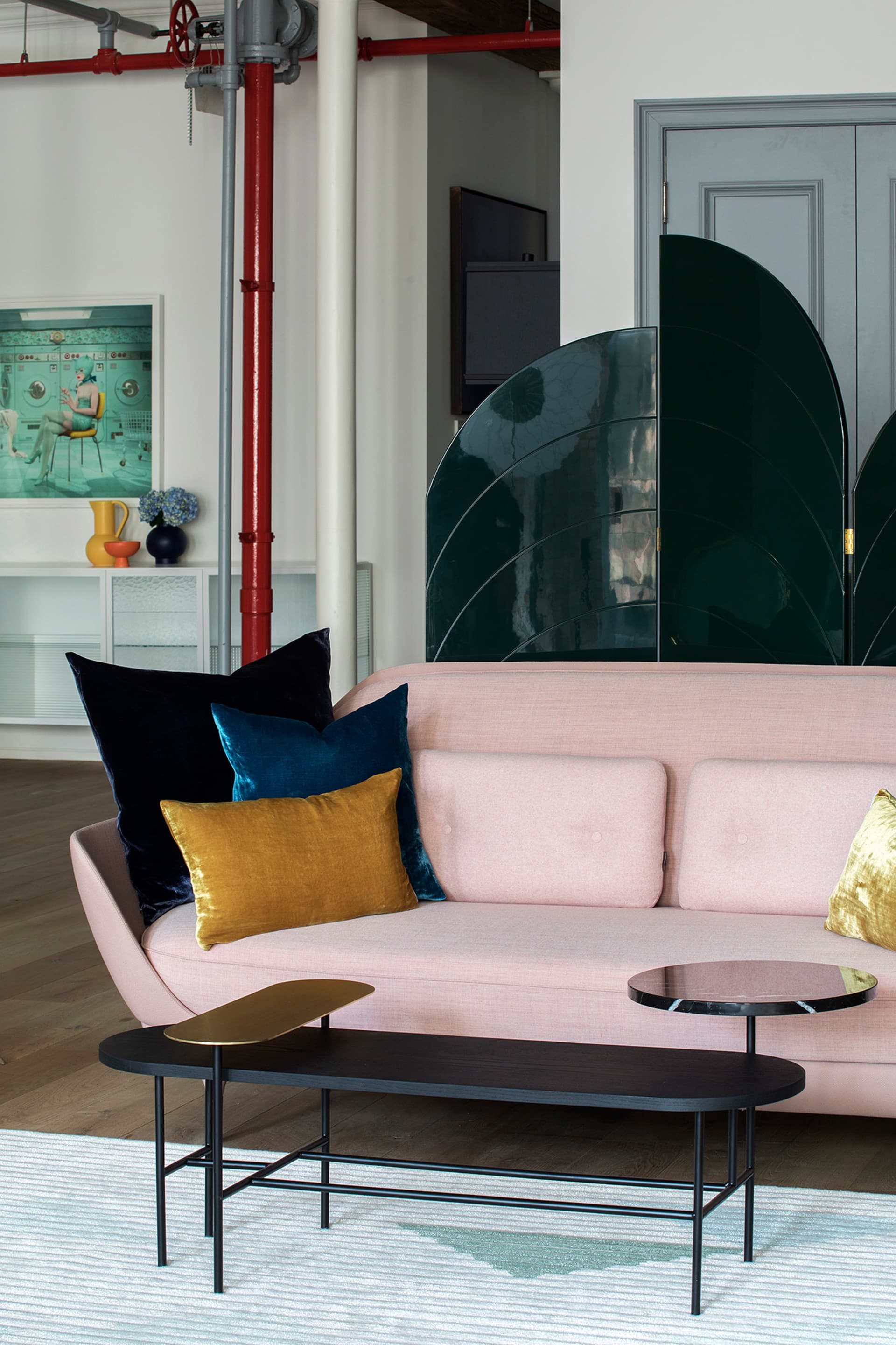 A modern living room featuring a pink couch with assorted cushions, a black metal coffee table with a golden tray, and a uniq