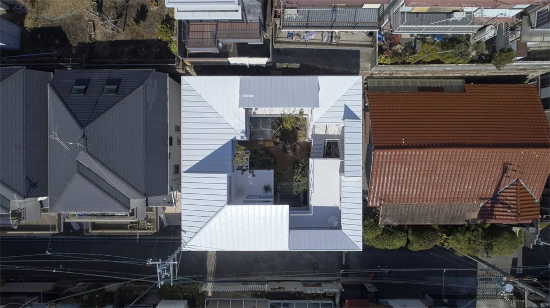 A white metal roof structure with an inner courtyard garden surrounded by modern residential houses.