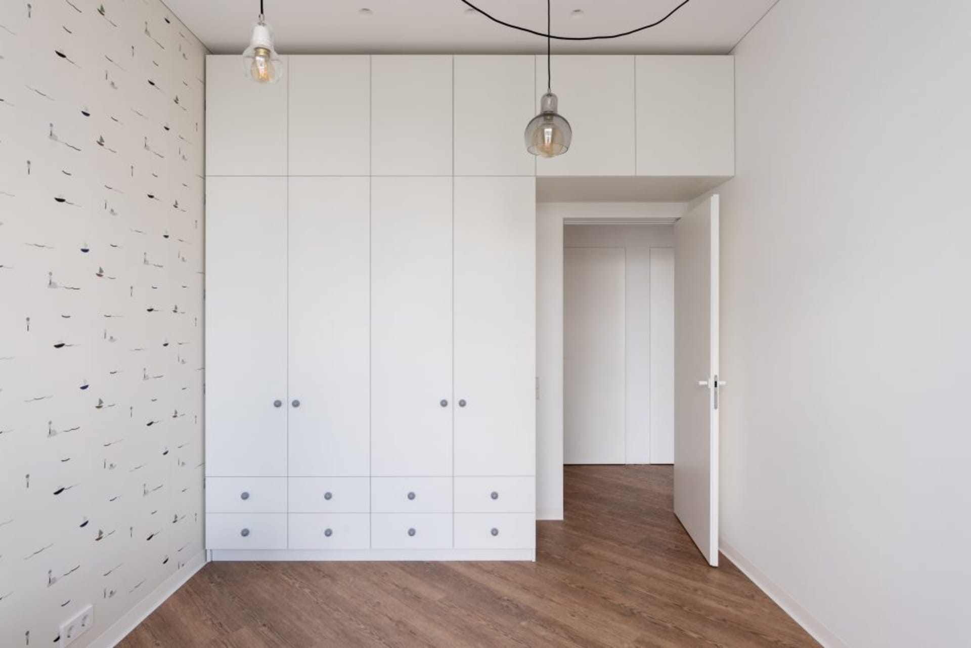 A modern bedroom featuring white cabinets, paper-patterned wallpaper, and hardwood floors.