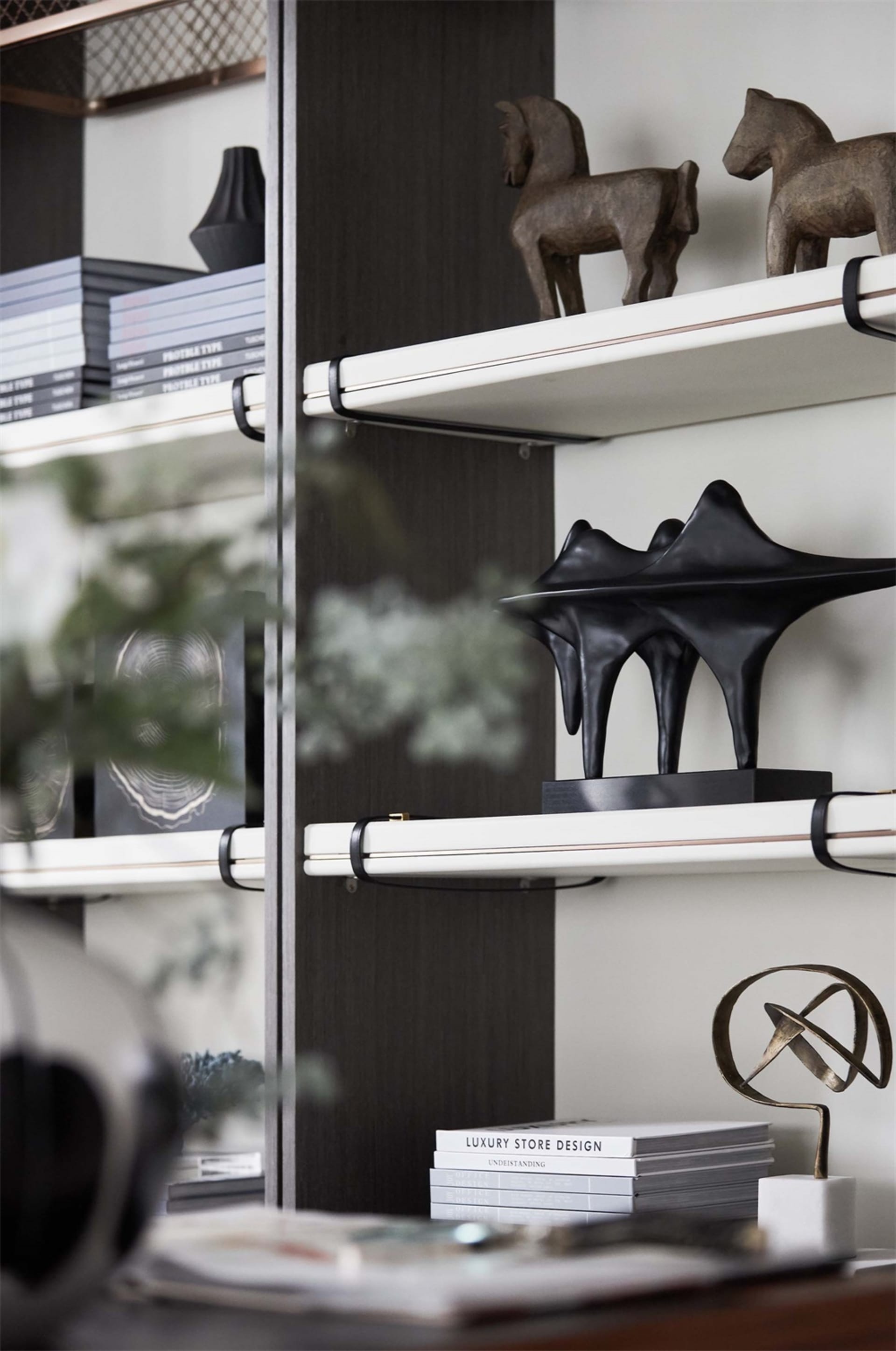 A modern metal shelf with books, horse sculptures, and abstract sculptures.