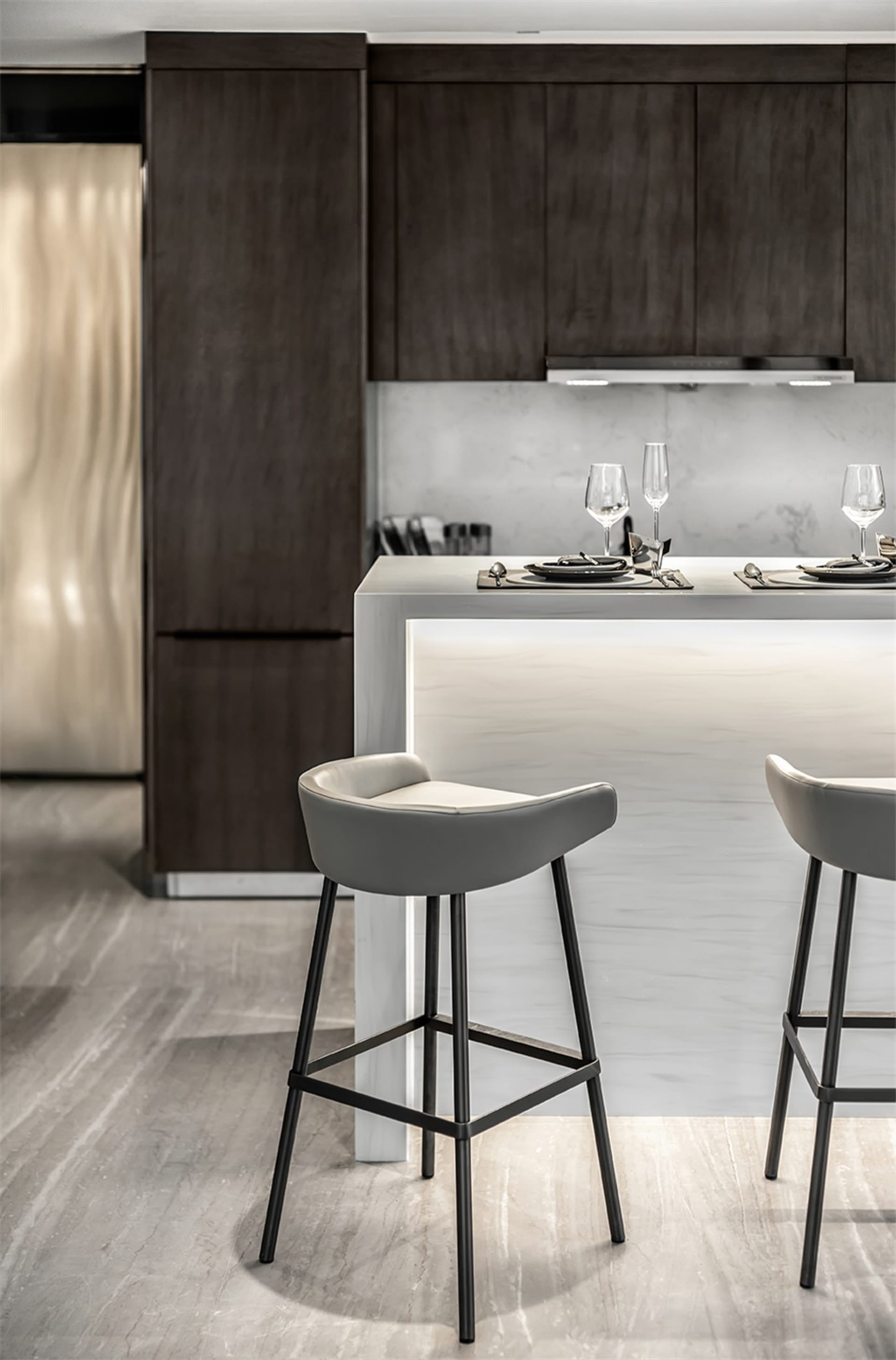 Modern kitchen with marble countertops and dark cabinets, featuring sleek bar stools and a minimalist design.