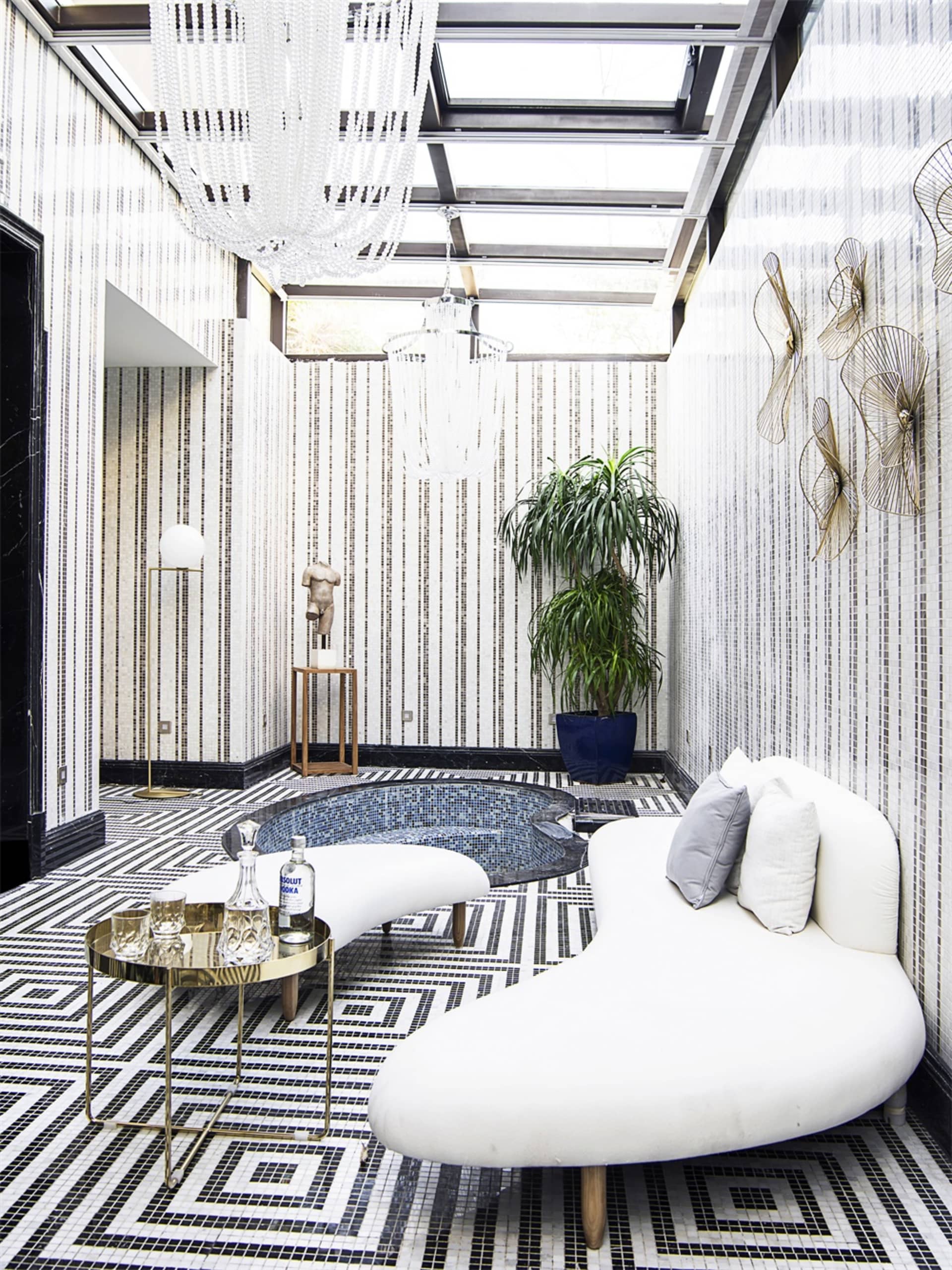 A modern living room with a white curvilinear sofa, a round metal table, a decorative floor lamp, and a large potted plant.