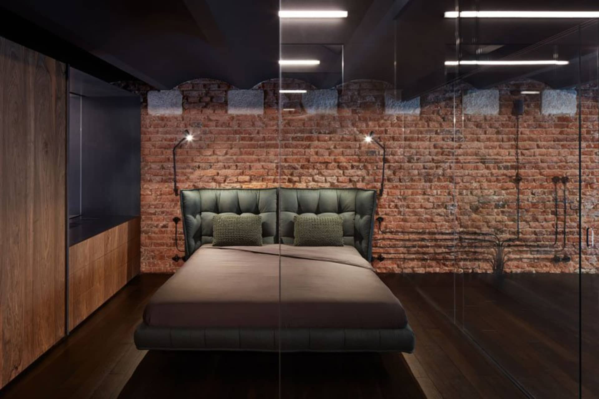 Modern bedroom with industrial design featuring a bed made of leather and metal, with a brick wall and wooden floor.