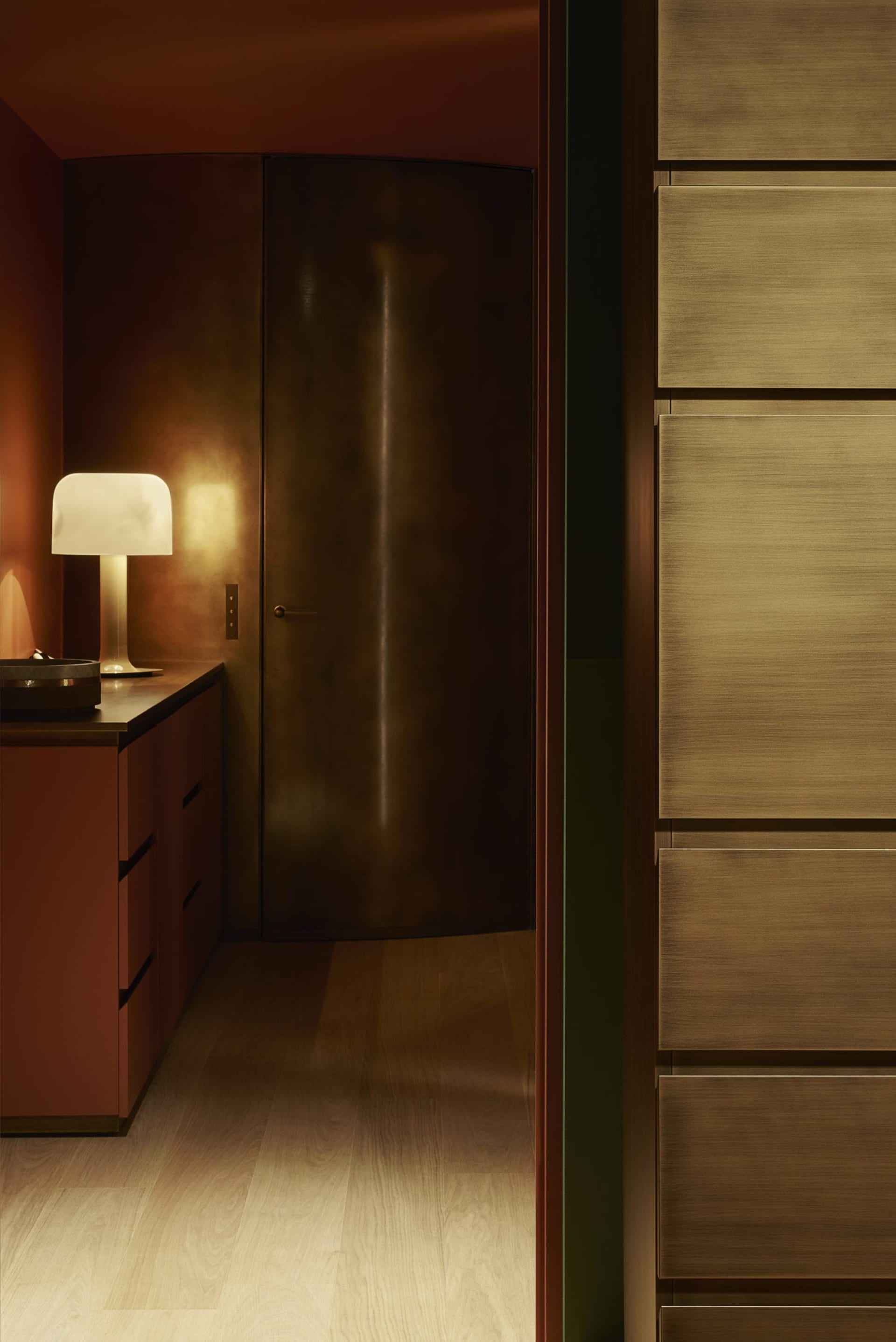 A modern kitchen with wood cabinets, featuring a table lamp with a white shade casting a warm glow on the wooden surfaces.