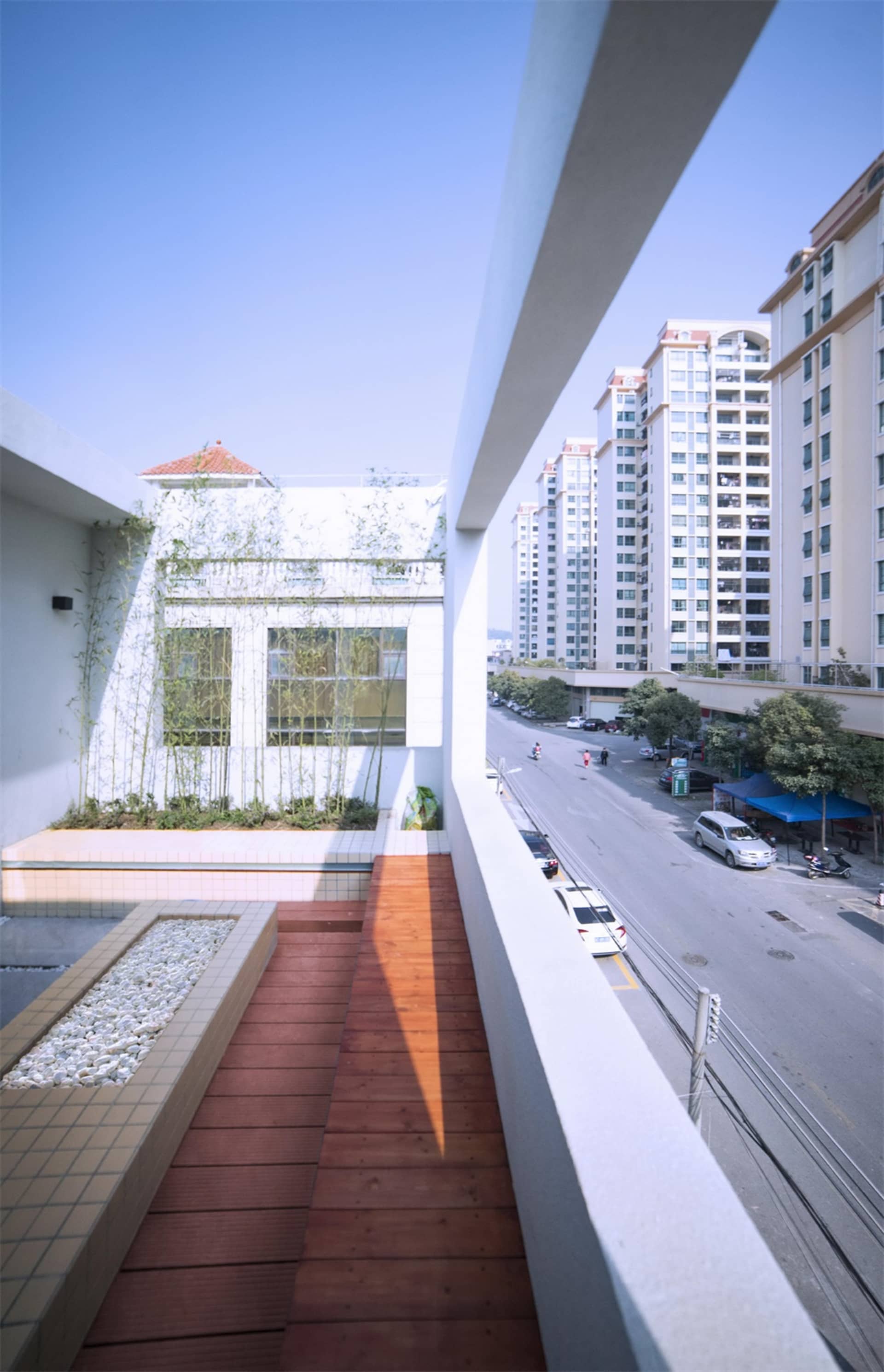 Concrete balcony with wooden floor next to a street with cars and buildings in the background.