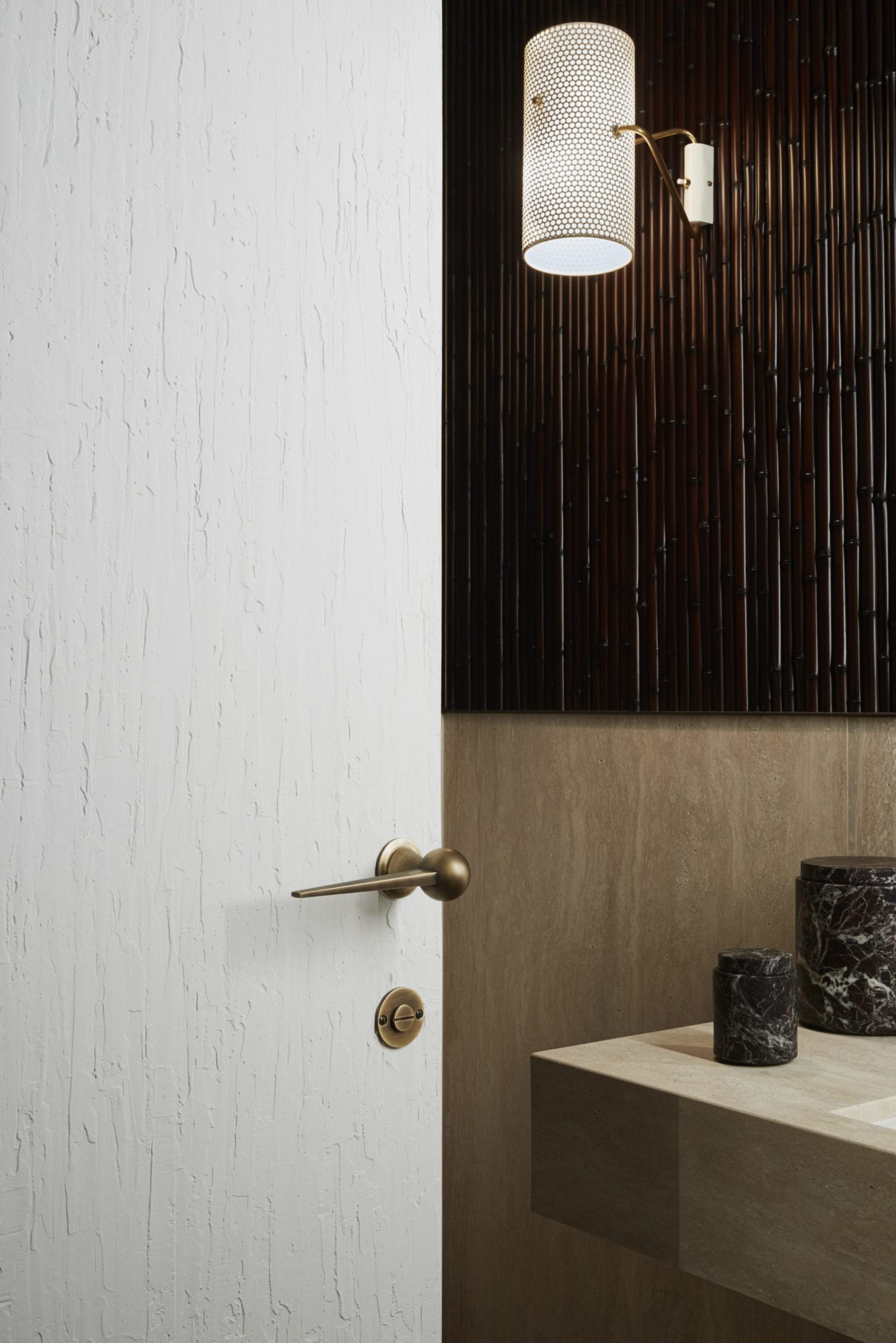 A modern minimalist bathroom featuring a white-painted wooden door with a sleek brass handle and a contemporary light fixture