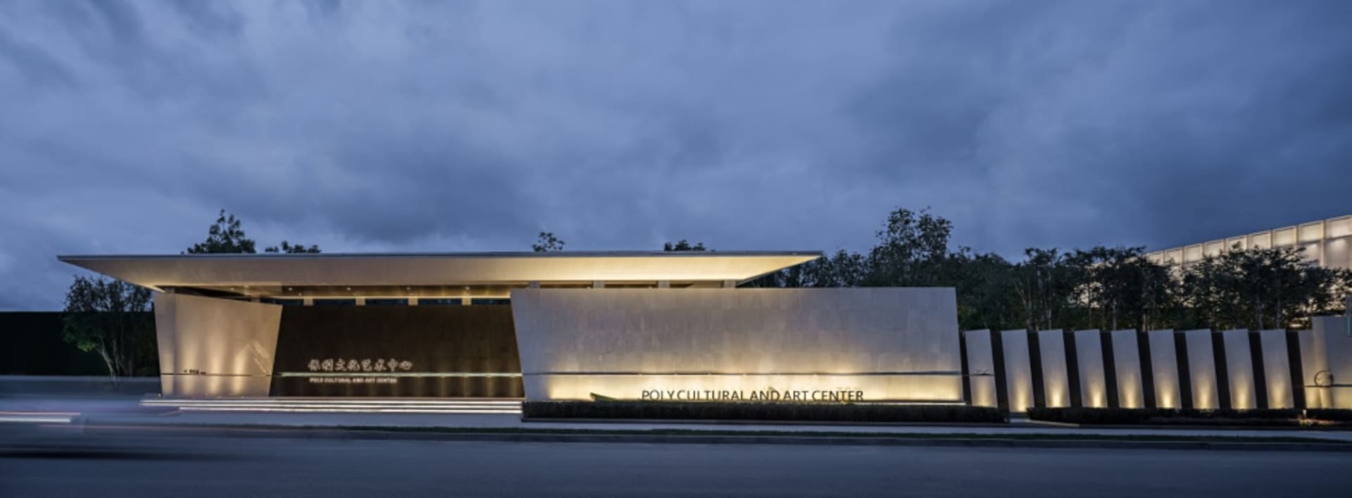 Evening view of the exterior of a modern cultural center with metal cladding and illuminated accents.
