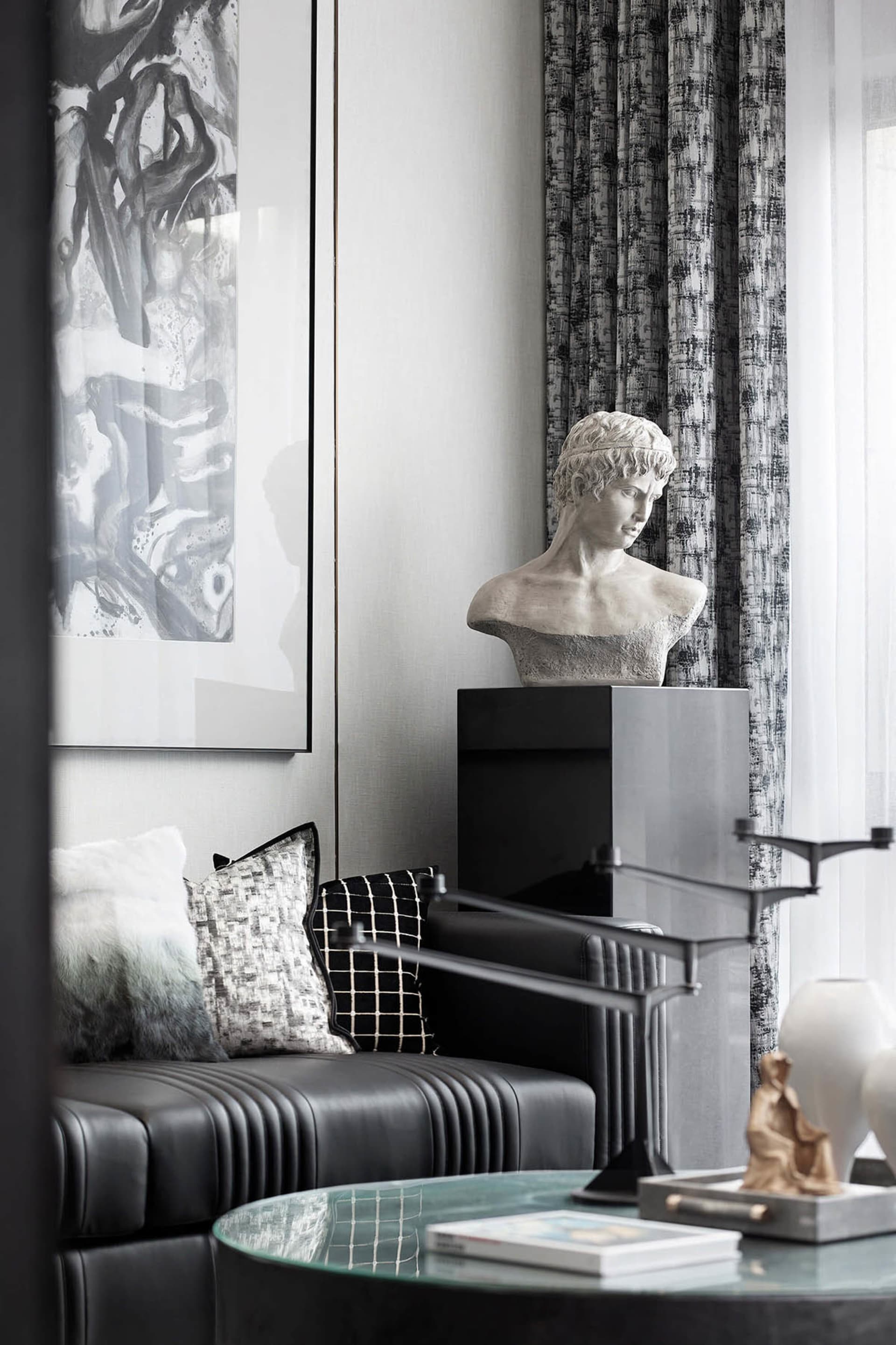 A modern living room featuring a metal and leather sofa with a black and white checkered cushion, a decorative bust, and a gl