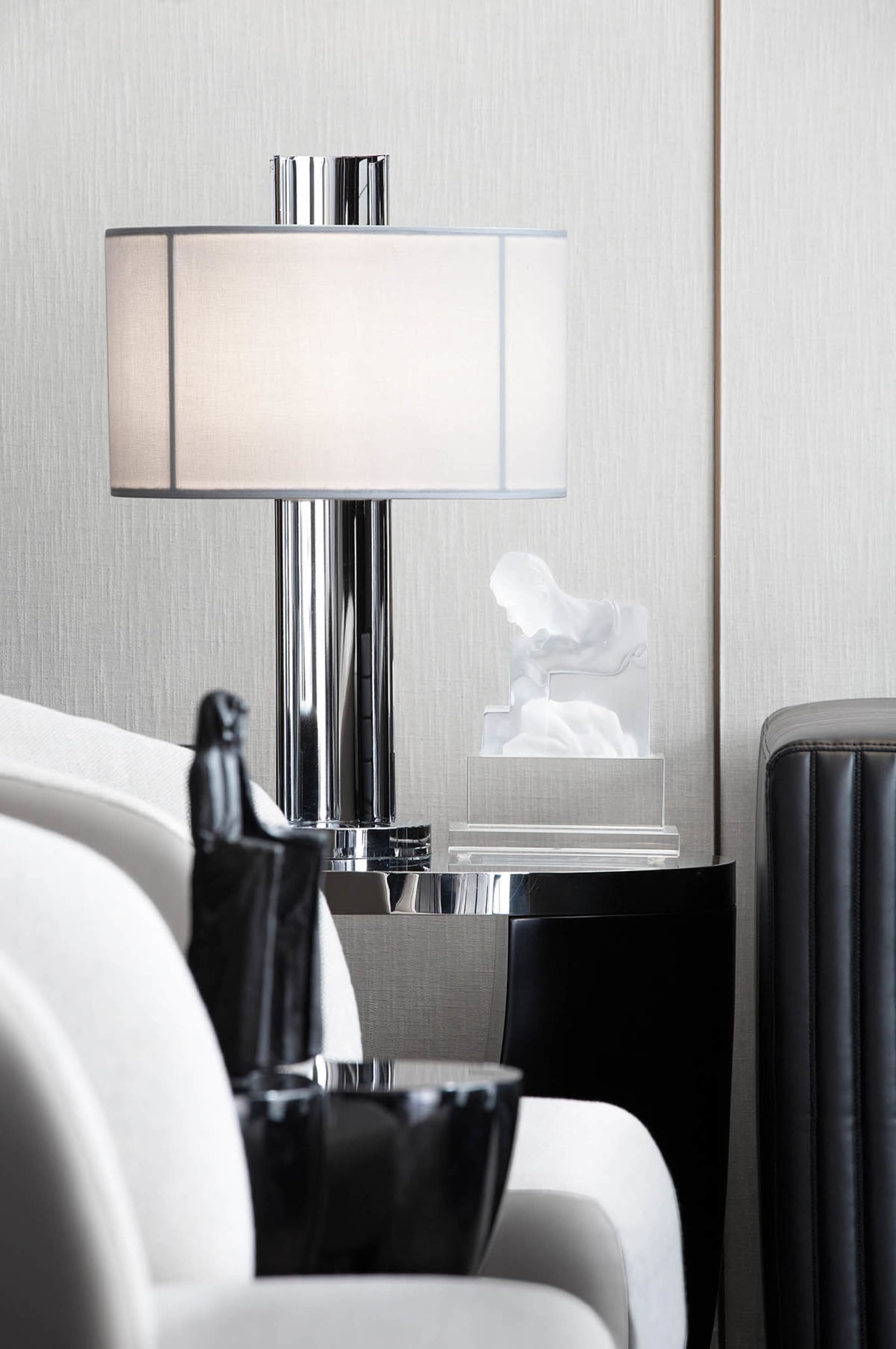 Modern lounge space featuring a glass and chrome table lamp with a white shade, accompanied by a transparent plastic sculptur