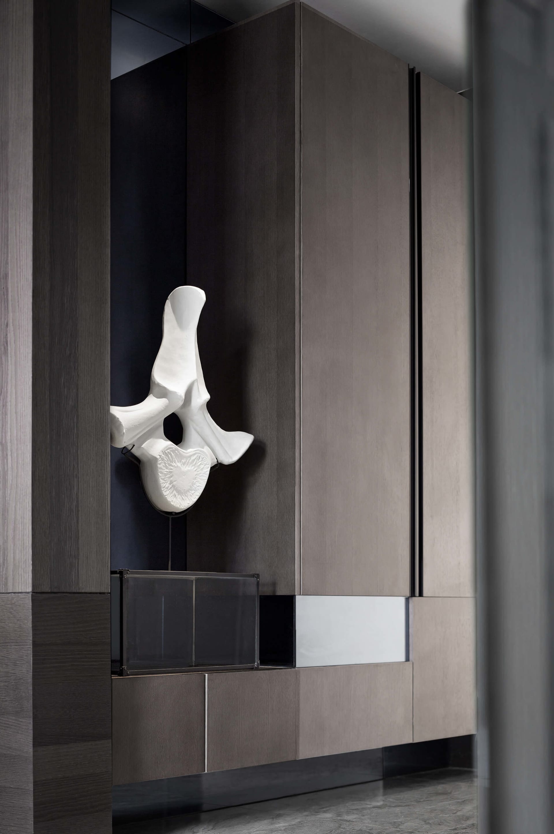 A stylish, modern minimalist dark wood display featuring a white sculptural piece placed above a sleek, minimalist cabinet.