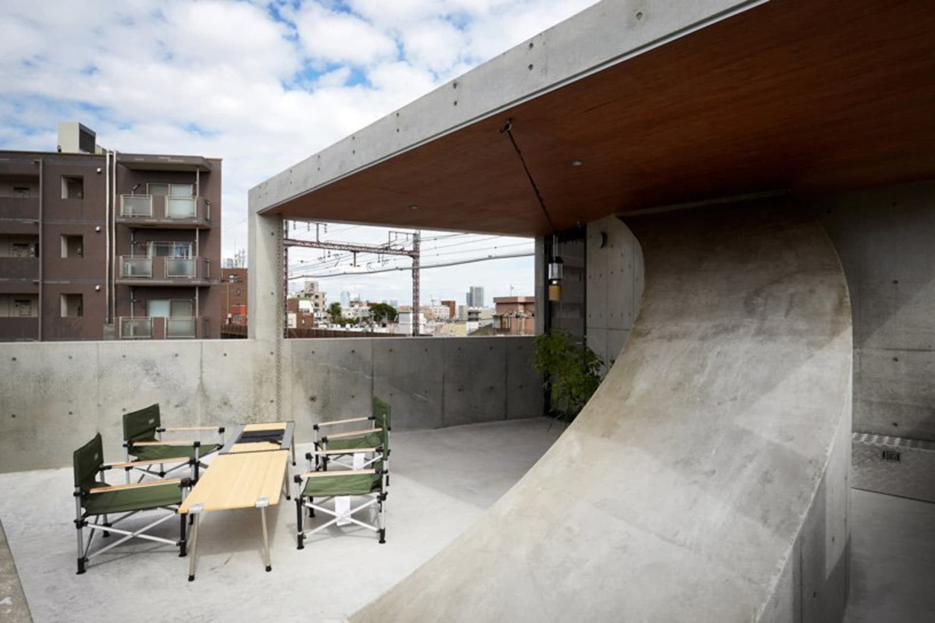Outdoor concrete rooftop with wooden table, chairs, and greenery