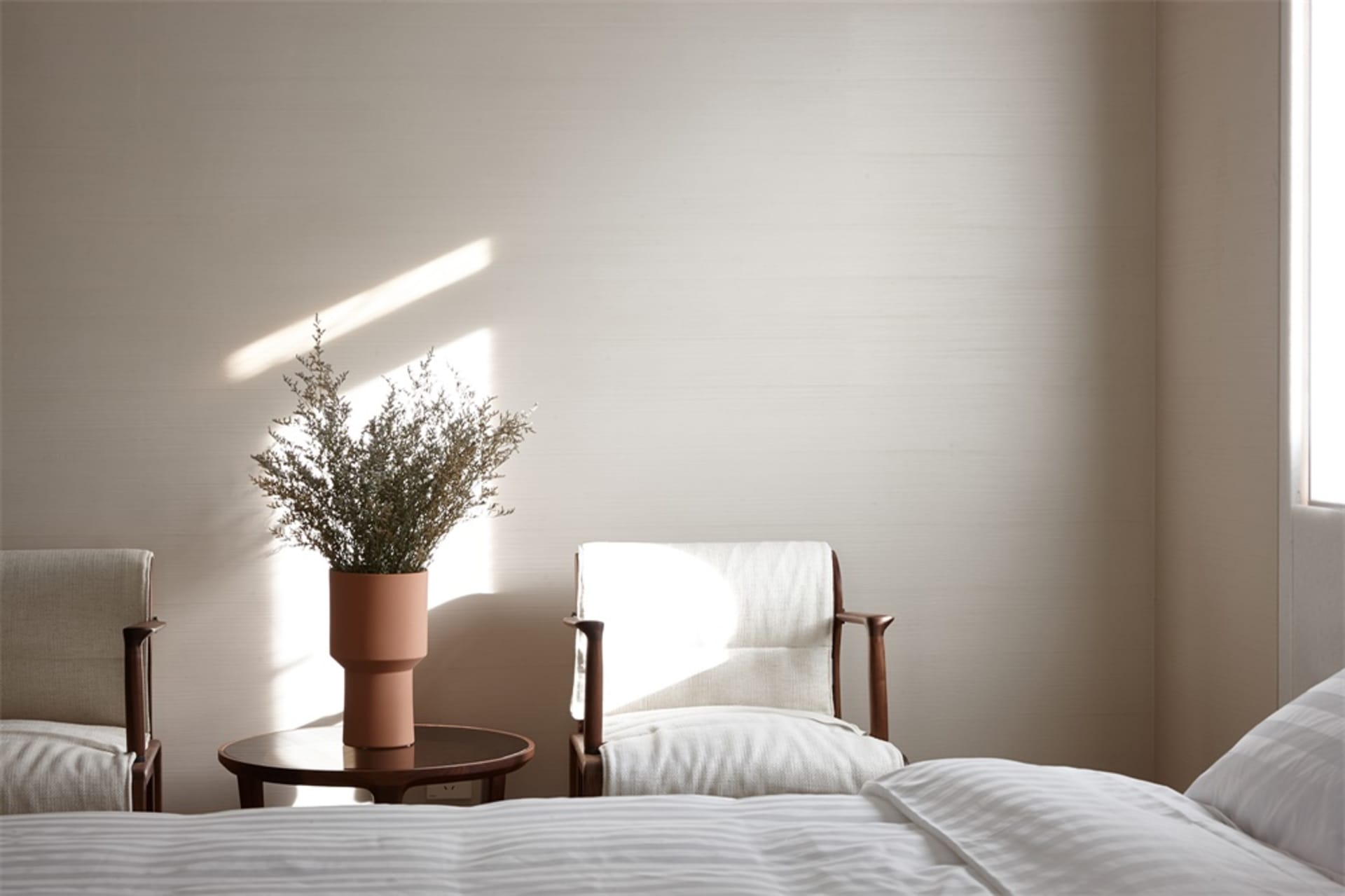 A minimalist residential room featuring fabric seating, wooden chairs with terracotta plant pots.