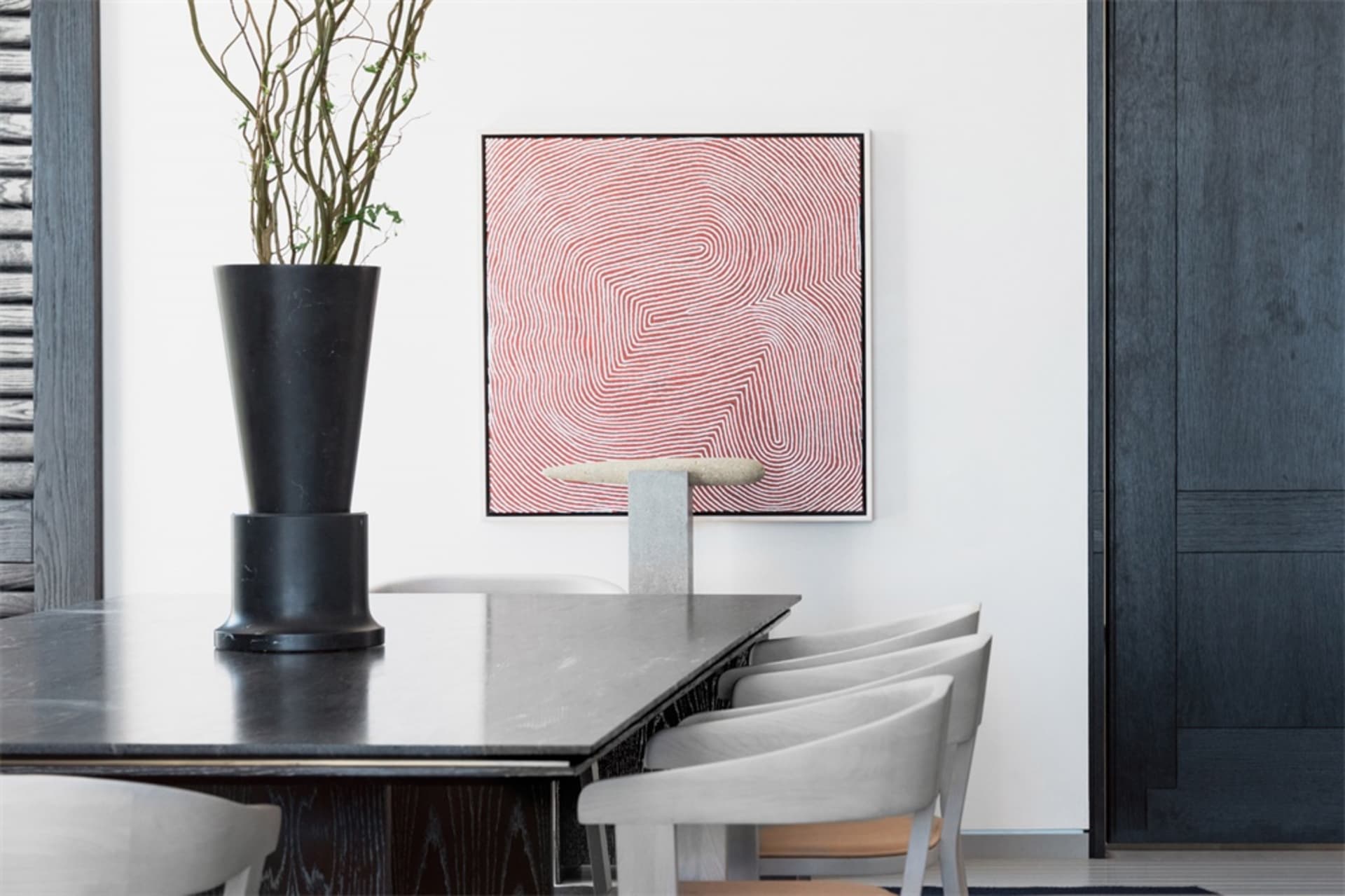 A modern dining table made of concrete with white chairs and a red and white abstract painting.
